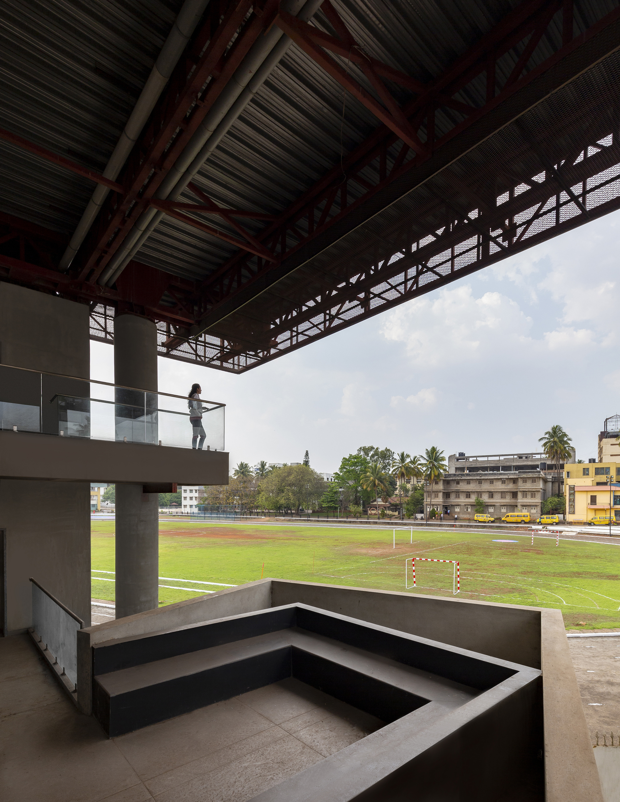 Covered terrace with concrete bleacher seating overlooking the football pitch under an exposed truss ceiling