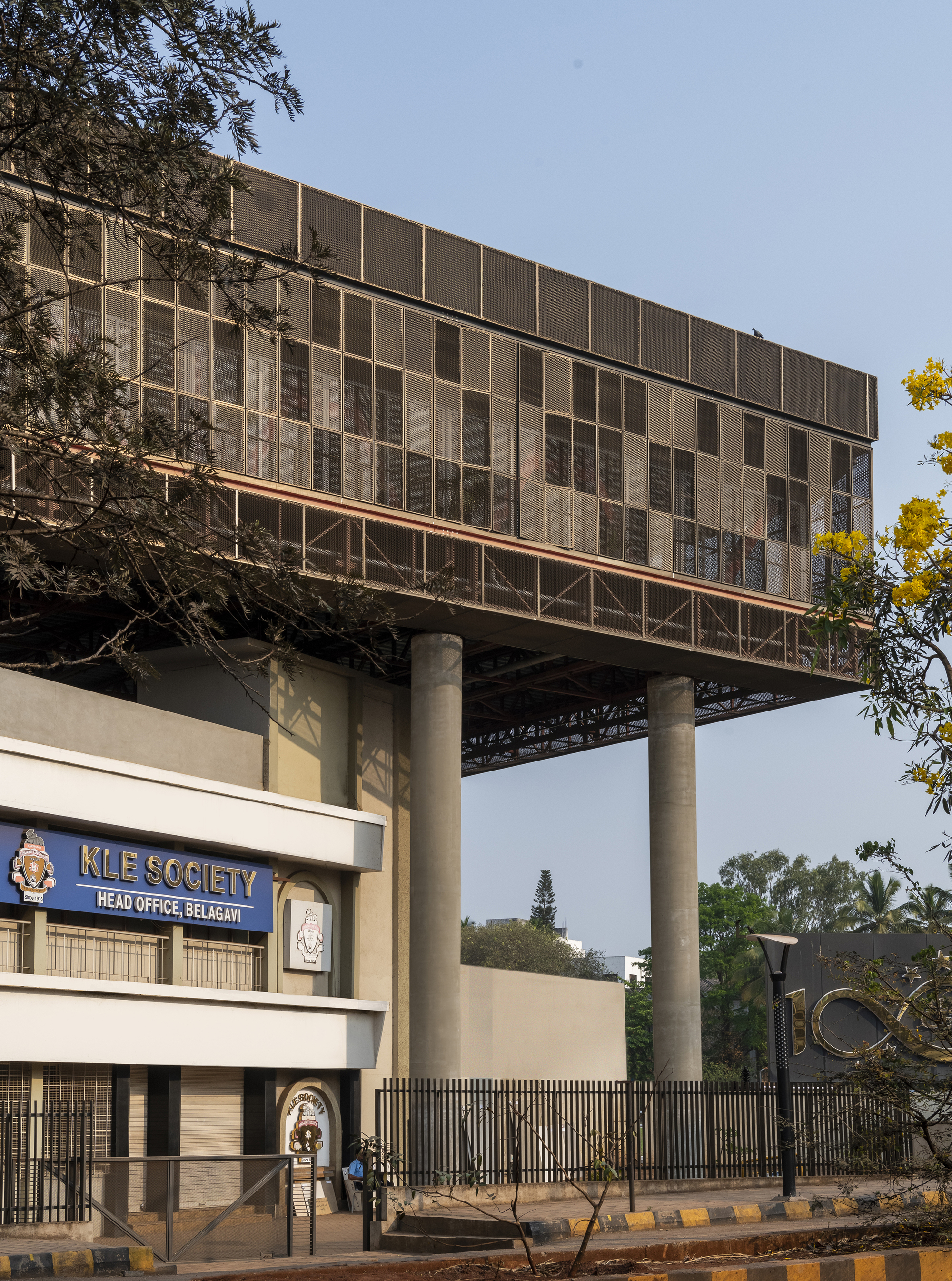 Street view showing the raised glass and panel facade on columns above an institutional entrance gate