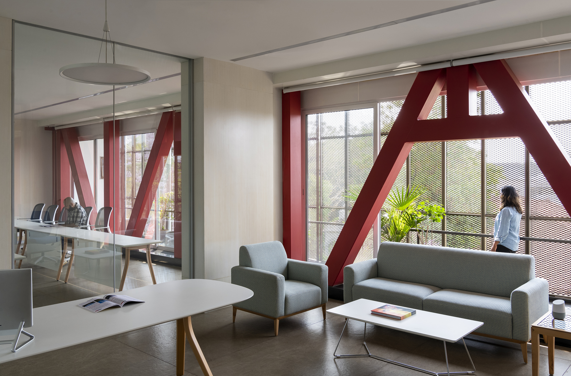 Lounge area with red diagonal steel bracing at glazed facade and a person standing by window