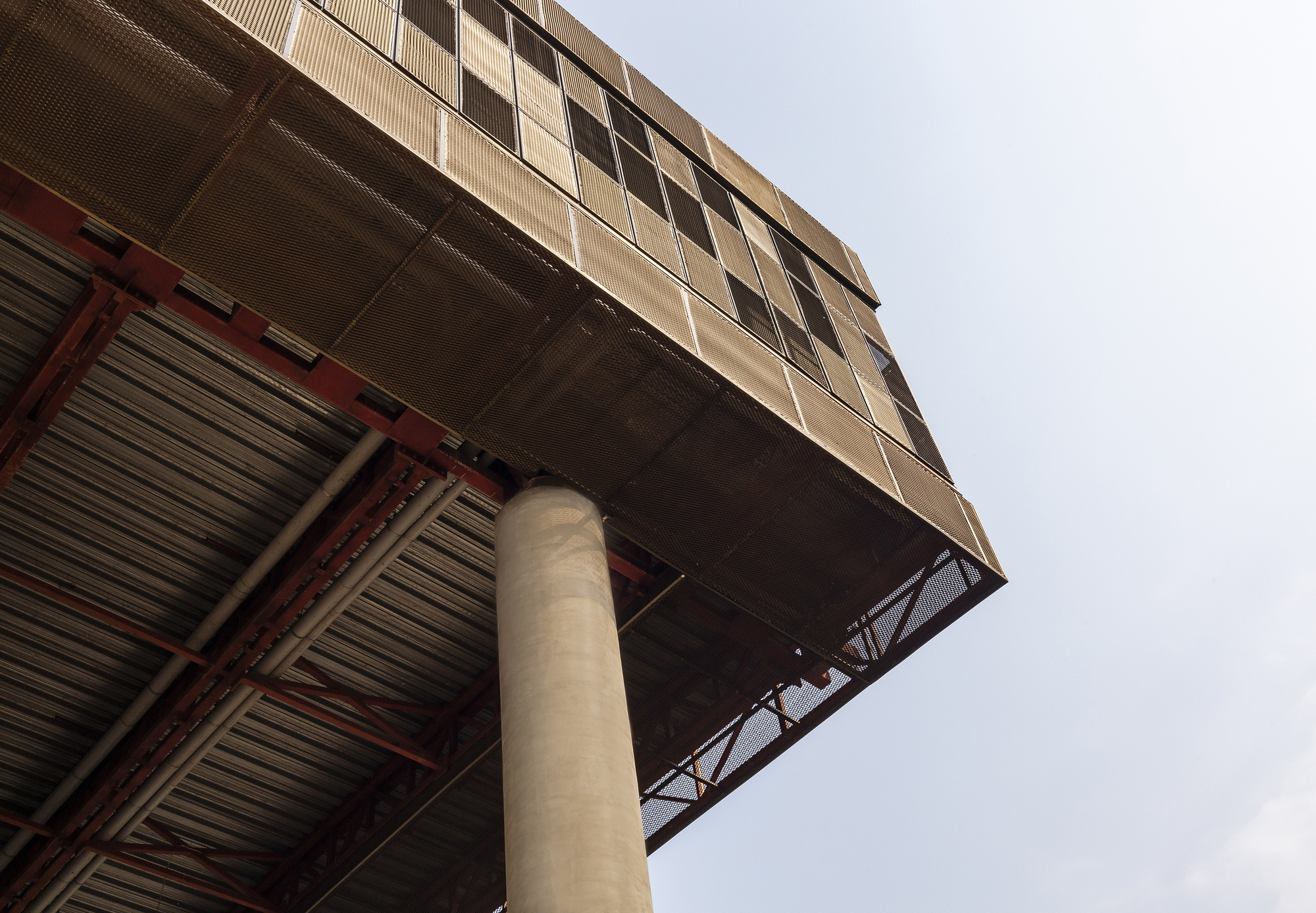 Upward view of cantilevered volume with exposed red steel trusses and concrete column