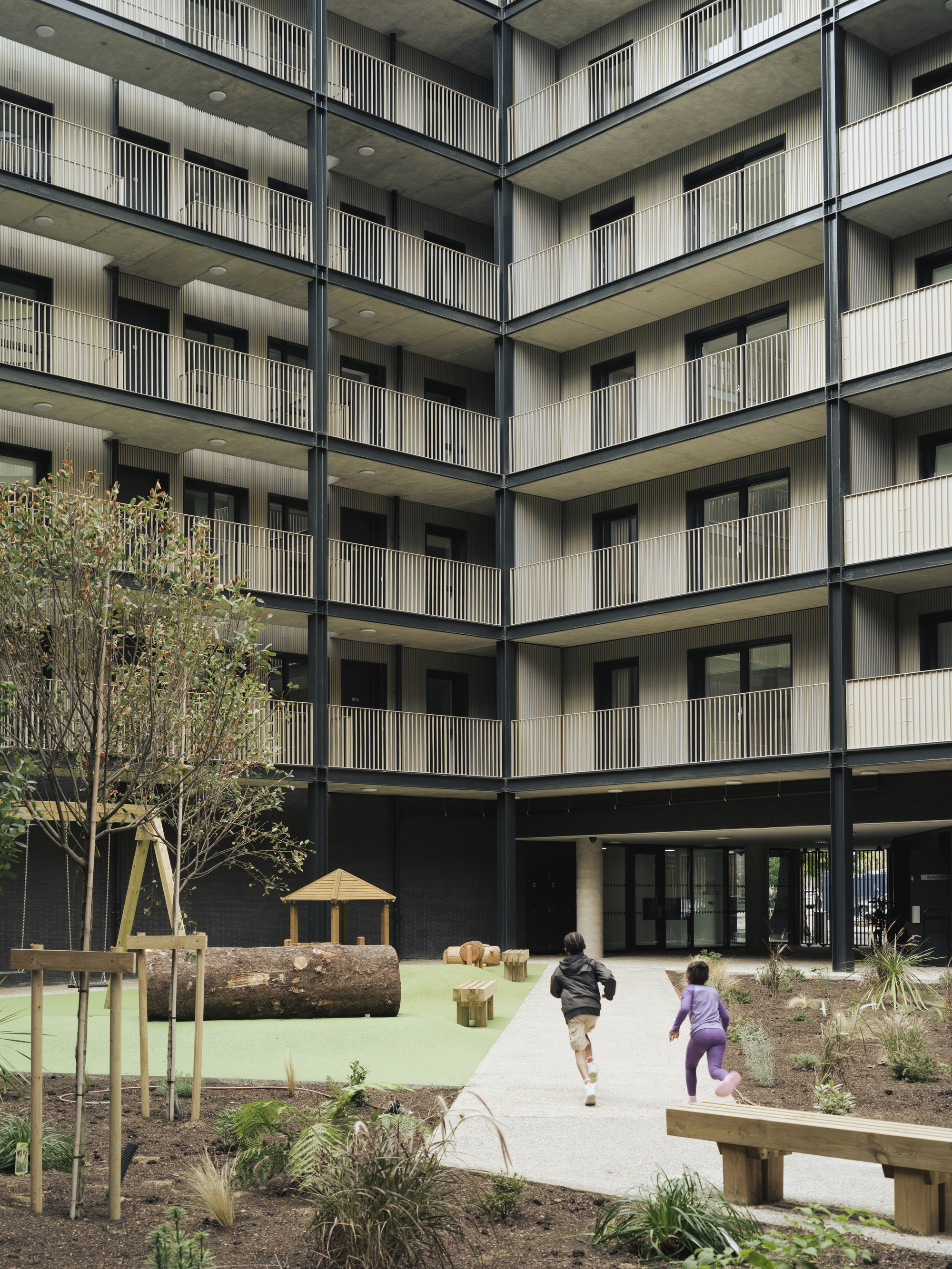 Interior courtyard with timber play structures and planted beds where two children are running