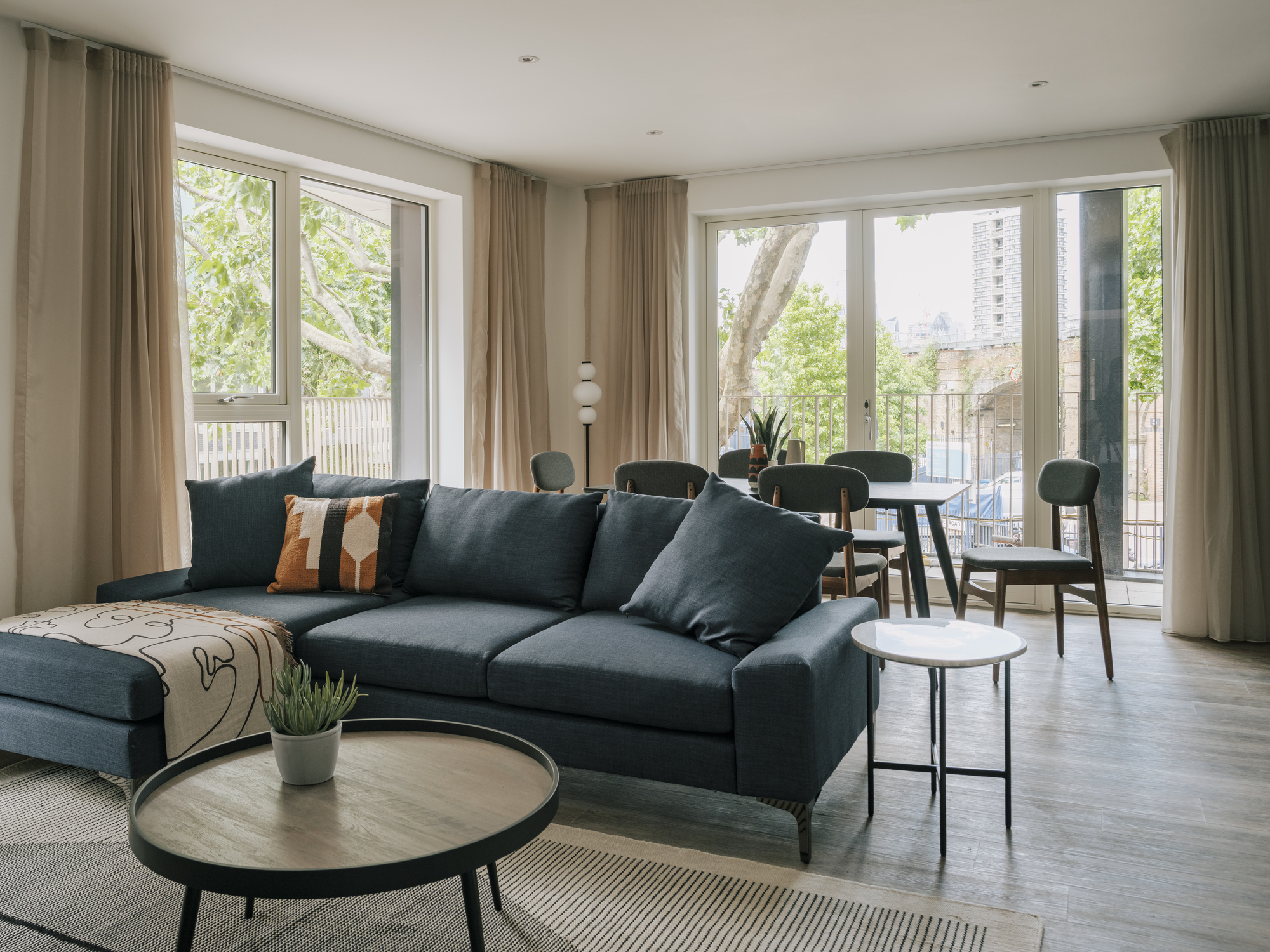 Living and dining area with floor-to-ceiling glazing opening onto a balcony with greenery beyond