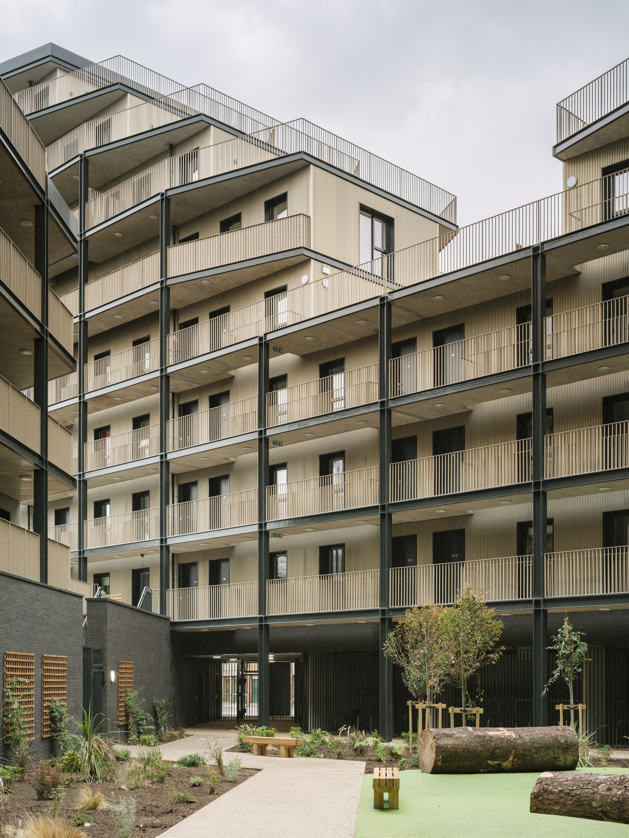 Shared courtyard with planted beds, young trees, and pale facades framing the communal space