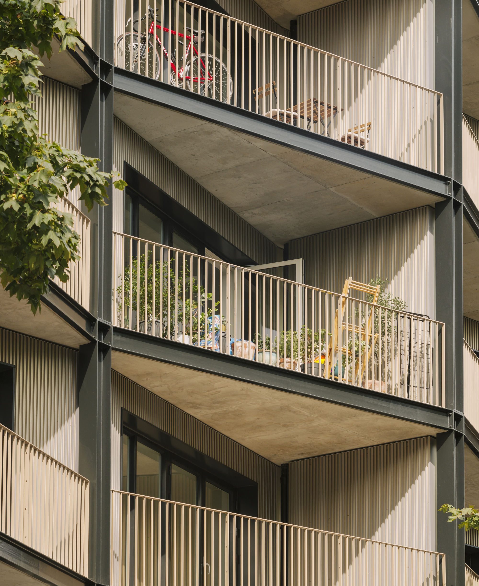 Close-up of stacked balconies with vertical metal railings and concrete soffits framed by tree branches