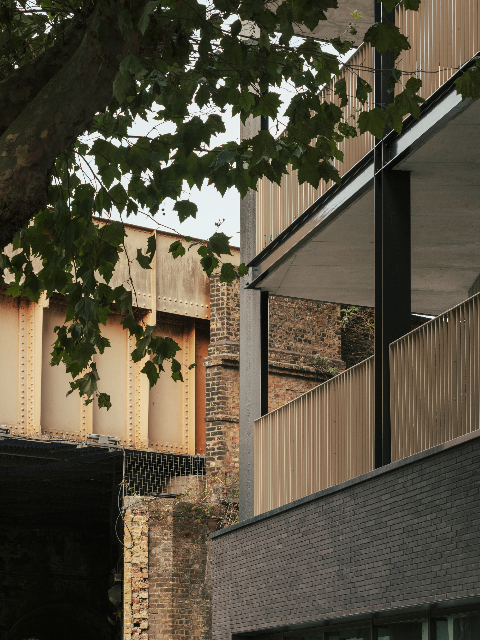 Corner detail where vertical metal cladding meets an adjacent brick wall under dense tree foliage