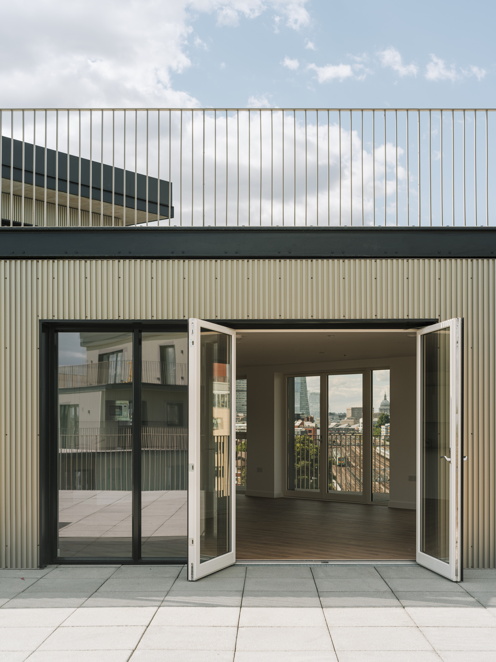Rooftop terrace with open folding glass doors leading into an apartment under a partly cloudy sky