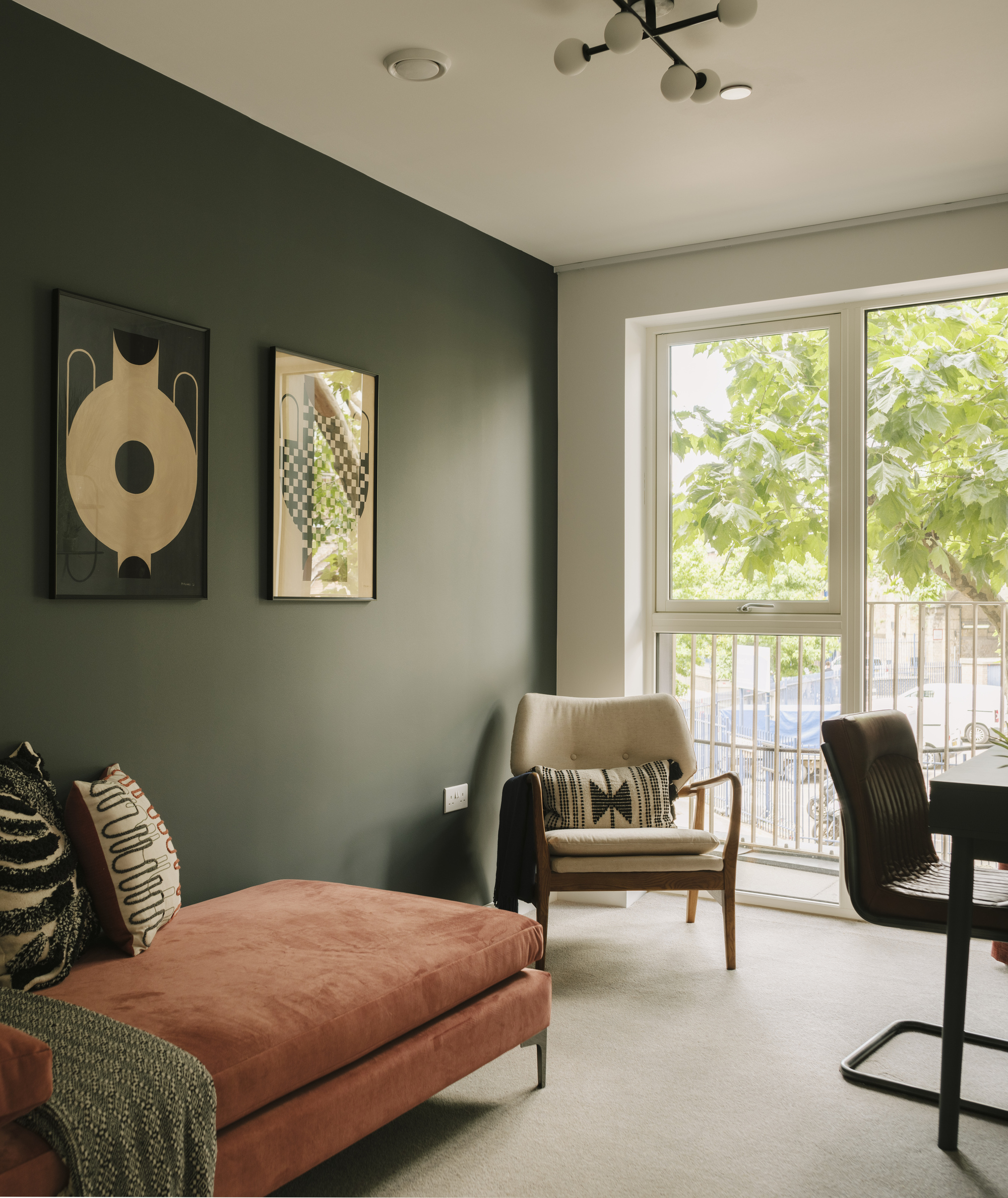 Corner seating area with a green accent wall, framed artwork, and a window with leafy tree views