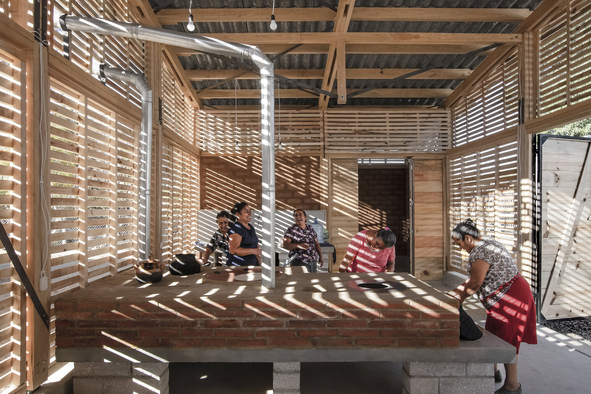 Raised brick platform with horizontal slatted timber screens filtering afternoon light onto seated children