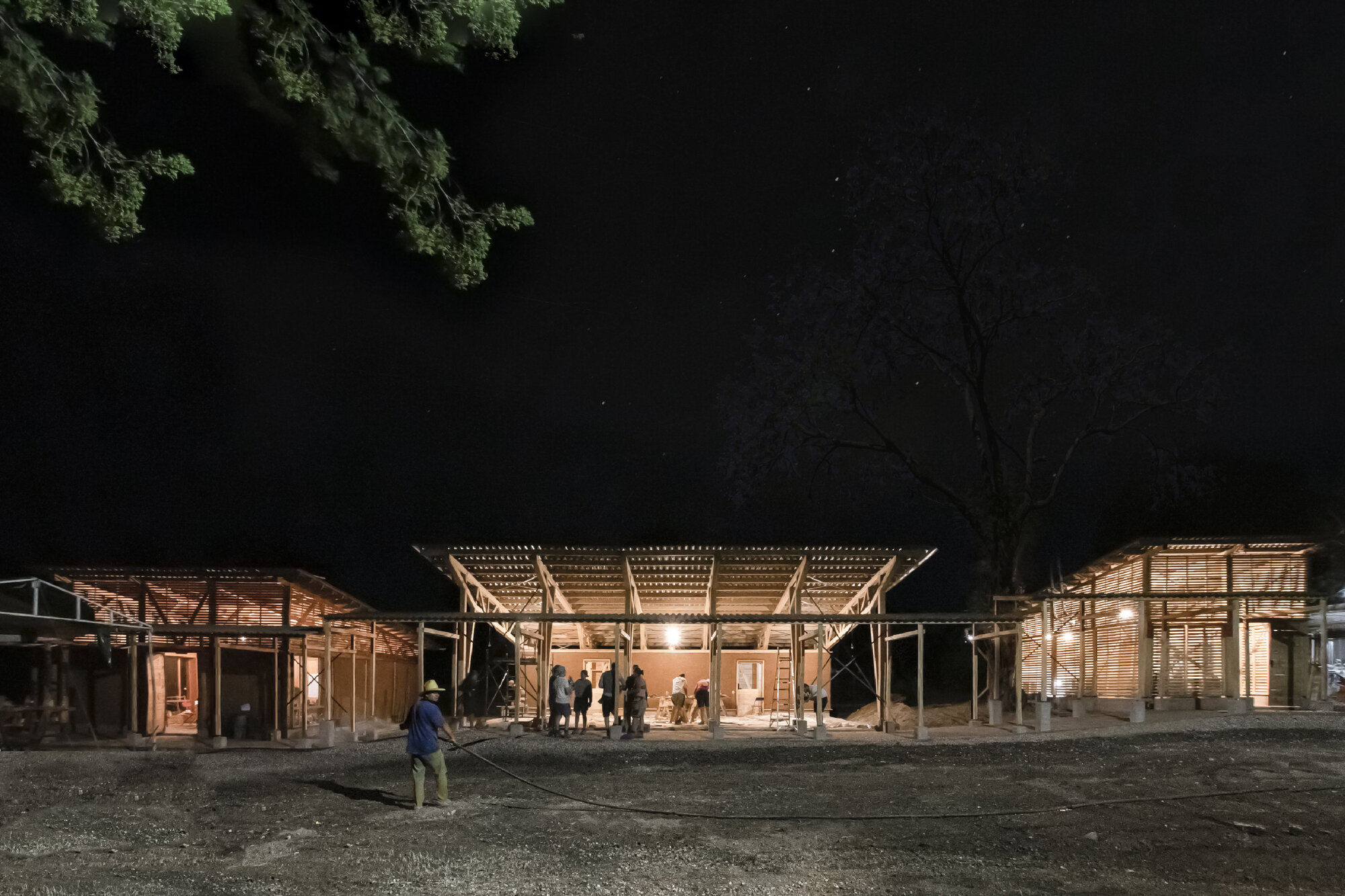 Night view of the illuminated timber pavilion complex beneath a starry sky with silhouetted trees