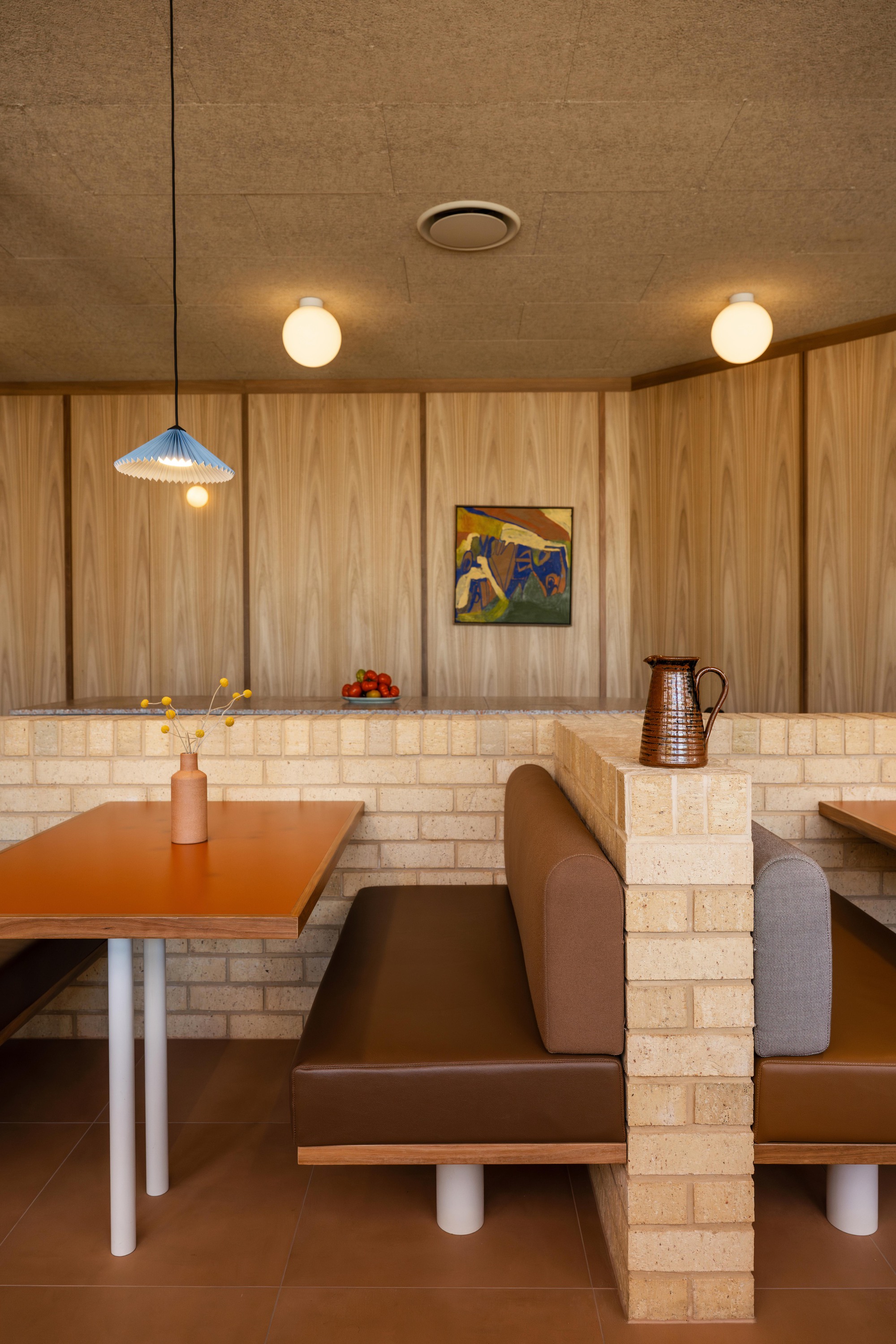 Booth seating with pale brick divider walls and timber paneling illuminated by globe pendants