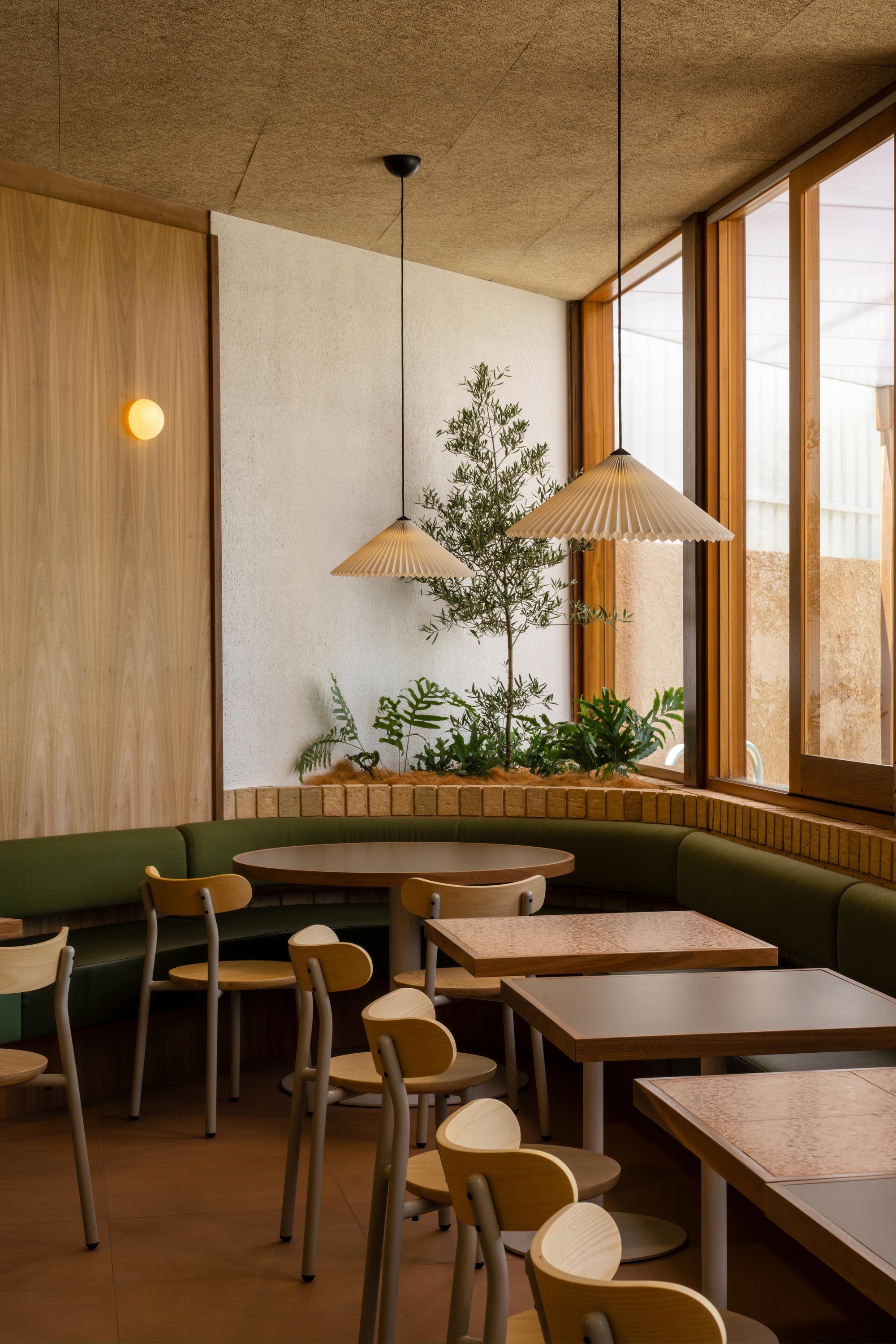 Corner banquette with planted bed beneath timber-framed window and pleated pendant lights