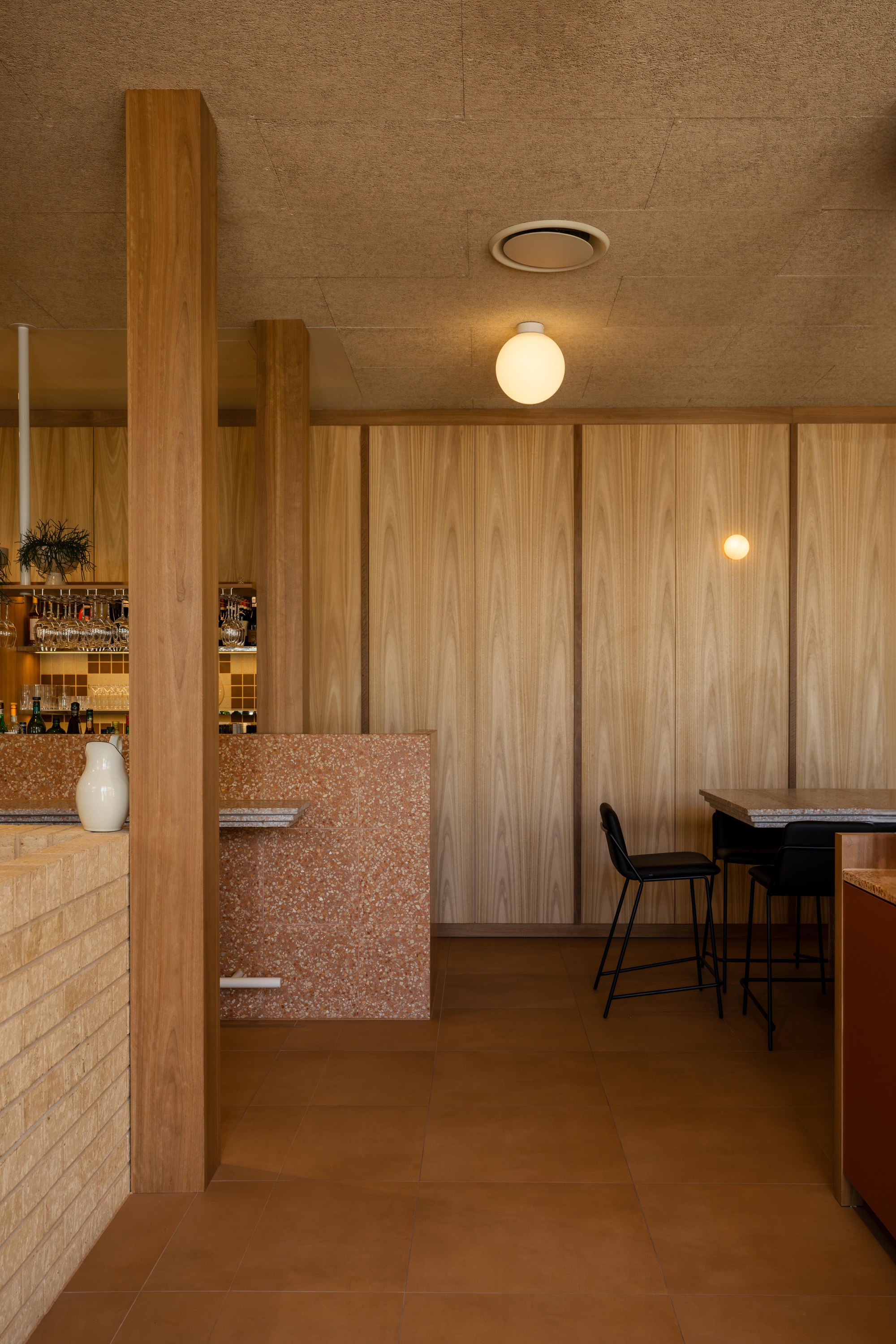 Passageway view toward bar seating with timber columns and terrazzo wall detail