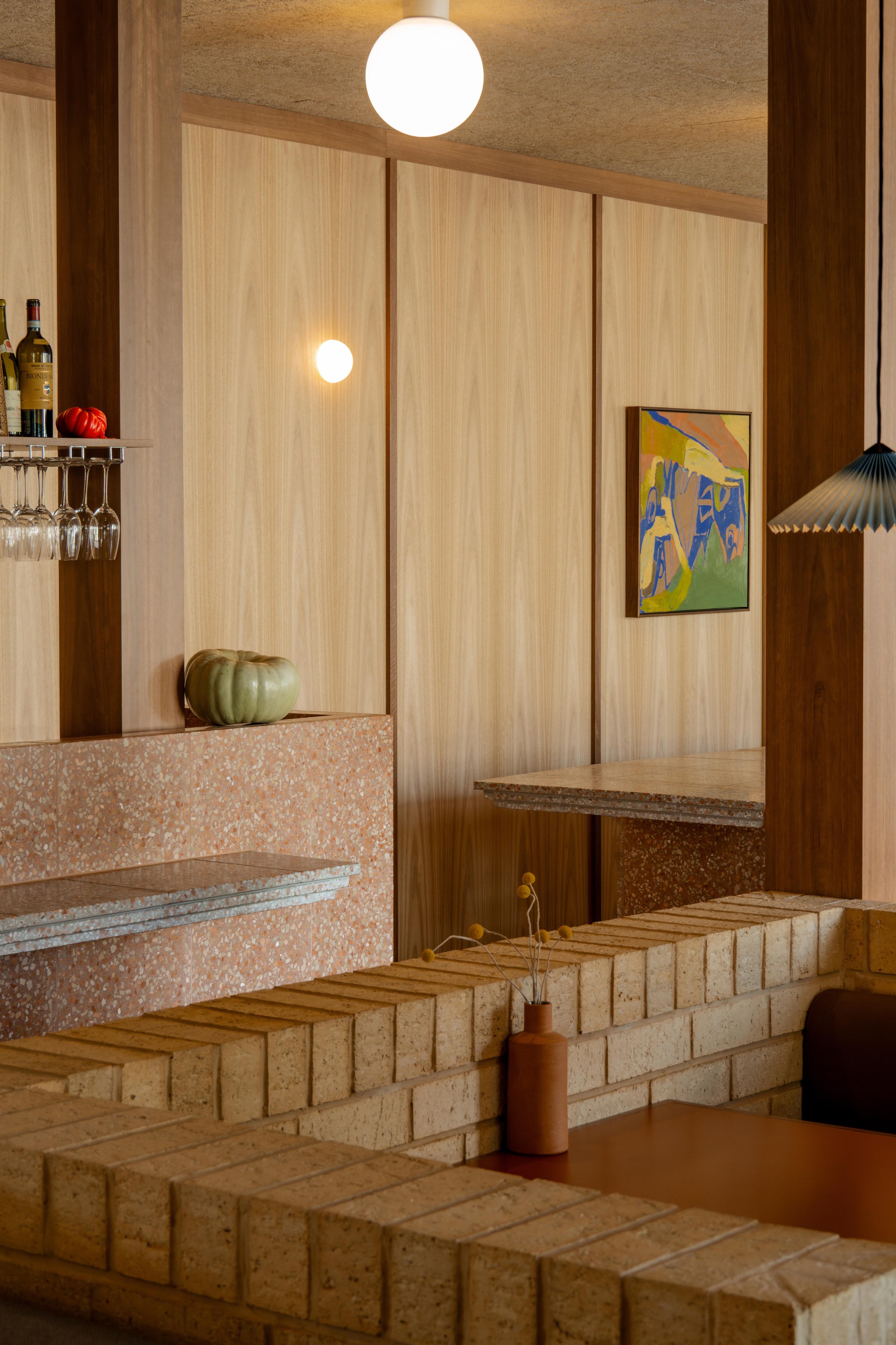 Terrazzo bar counter with integrated seating steps and light timber paneling under warm pendant lighting
