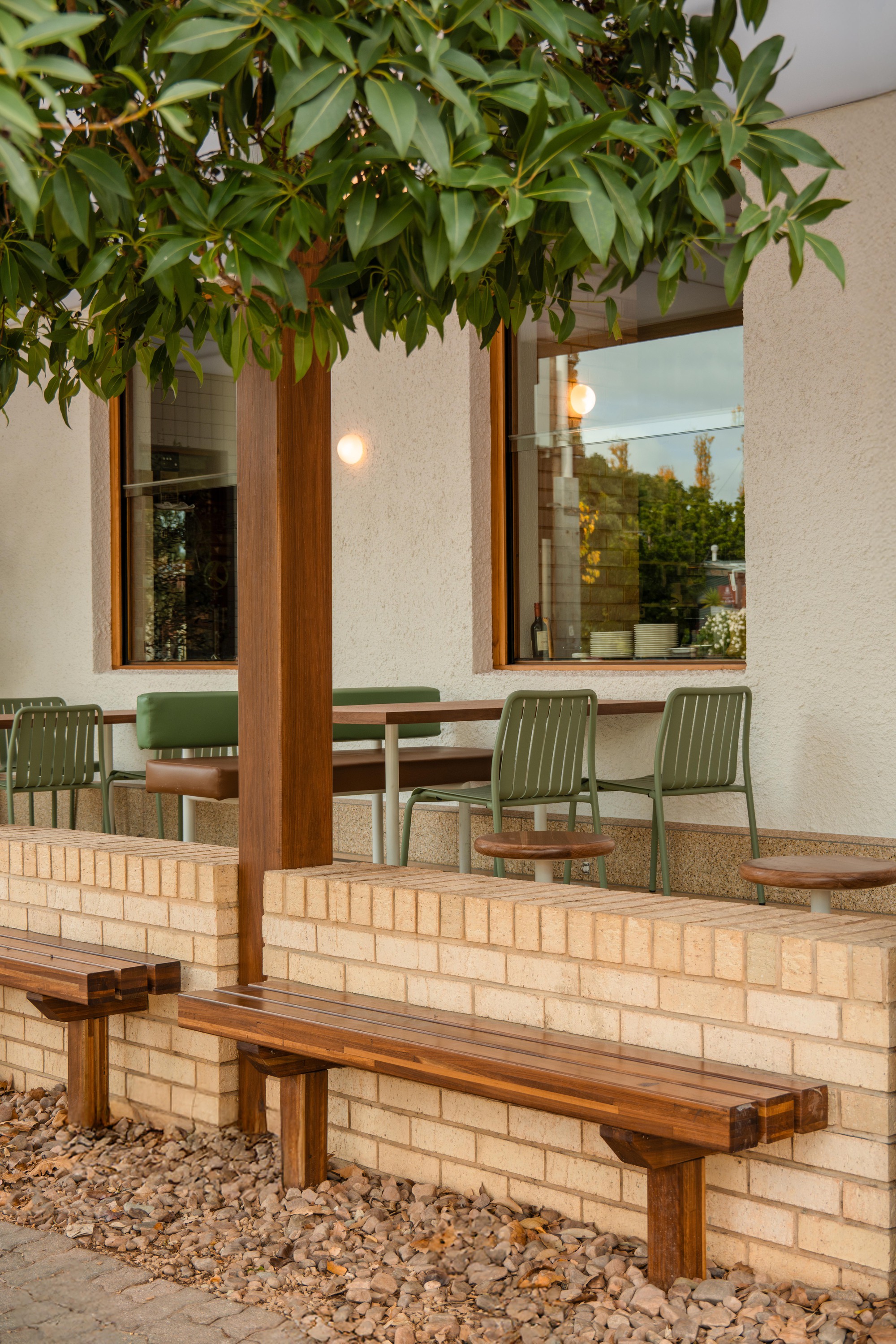 Outdoor seating area with cream brick planter wall and timber bench beneath overhanging foliage