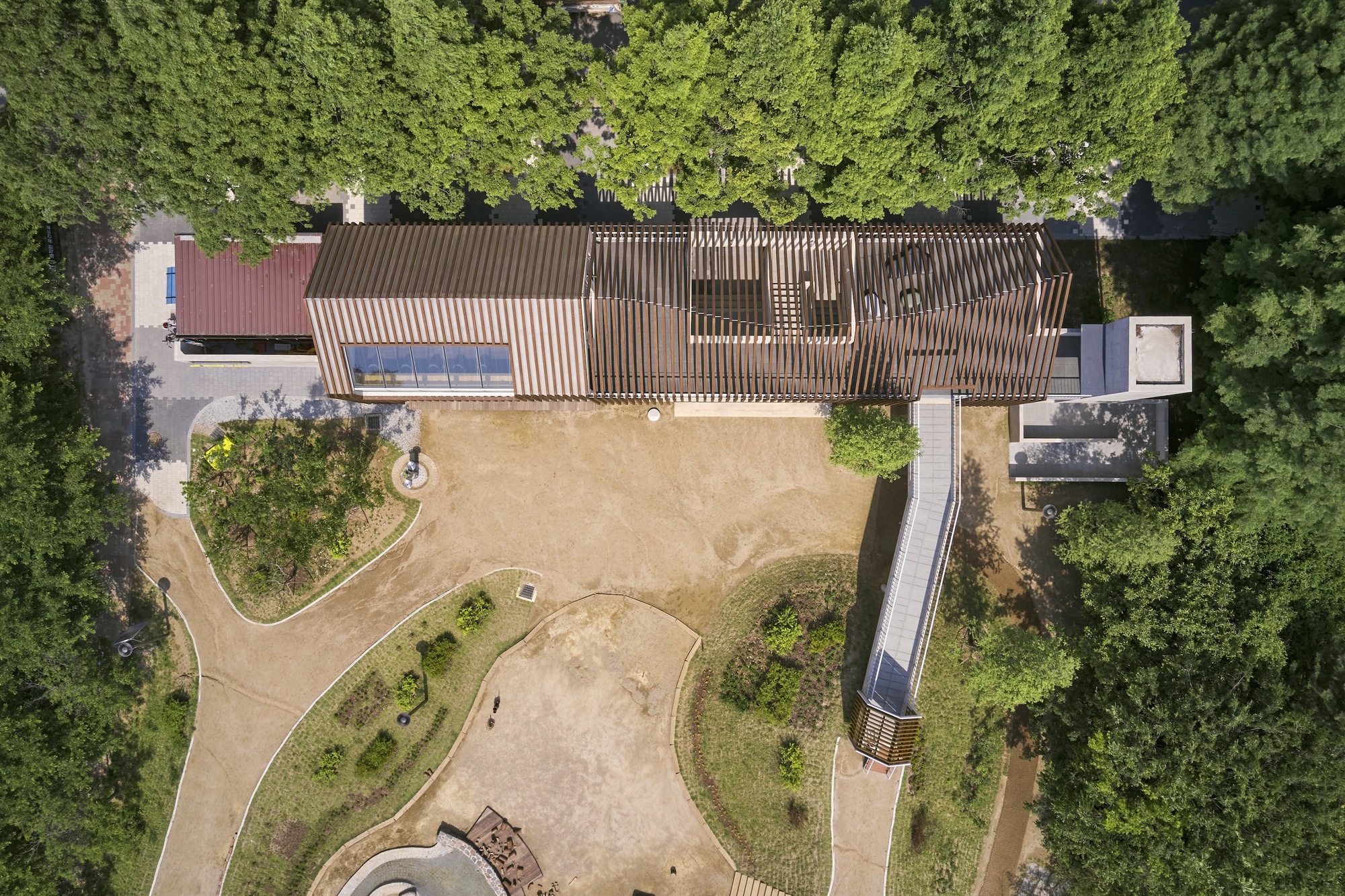 Overhead view showing the slatted timber roof canopy above a sandy courtyard edged with trees