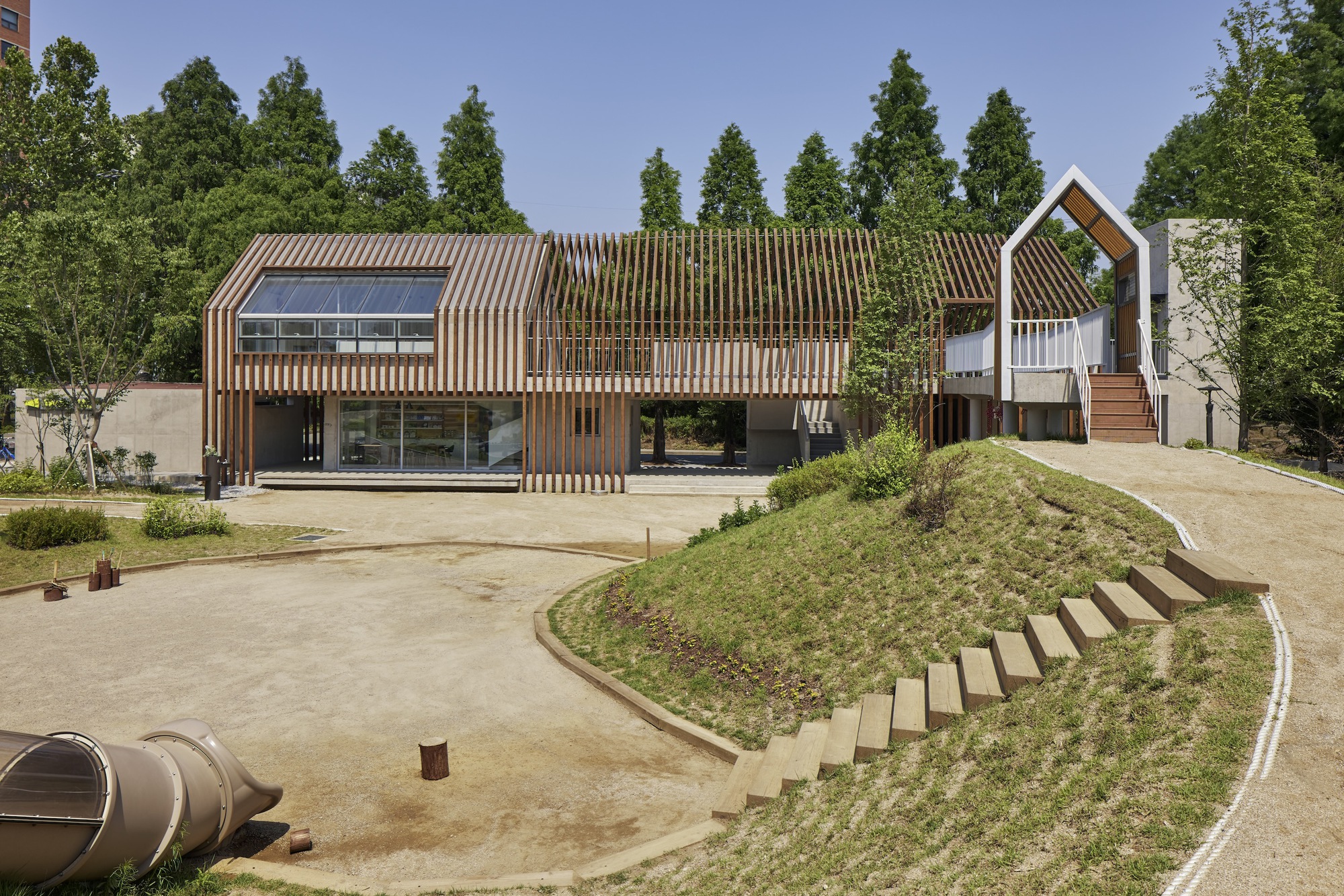 Front elevation with vertical timber slats screening the glazed facade and a house-shaped volume beyond