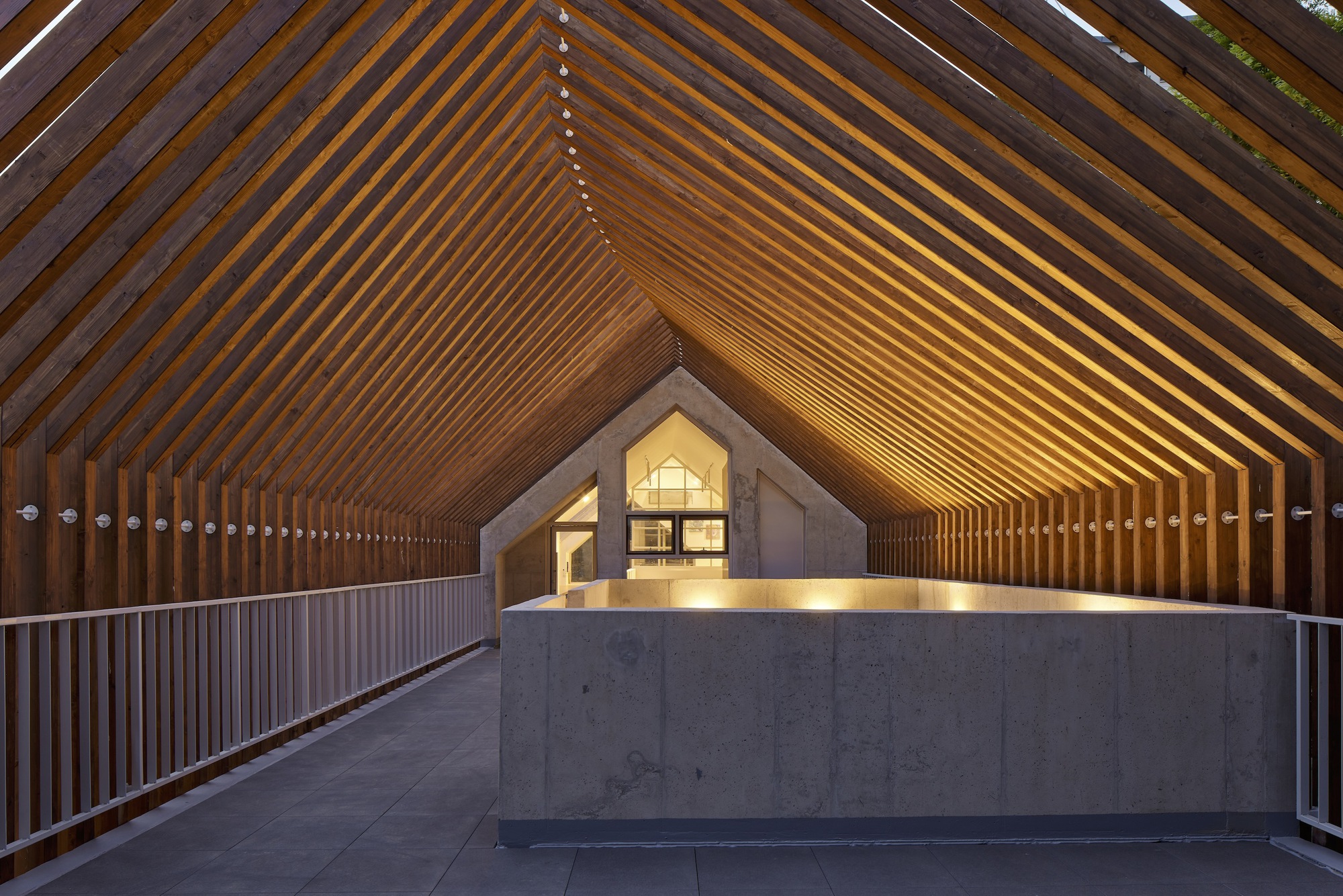 Covered walkway with rhythmic timber slat ceiling and concrete reception desk at twilight