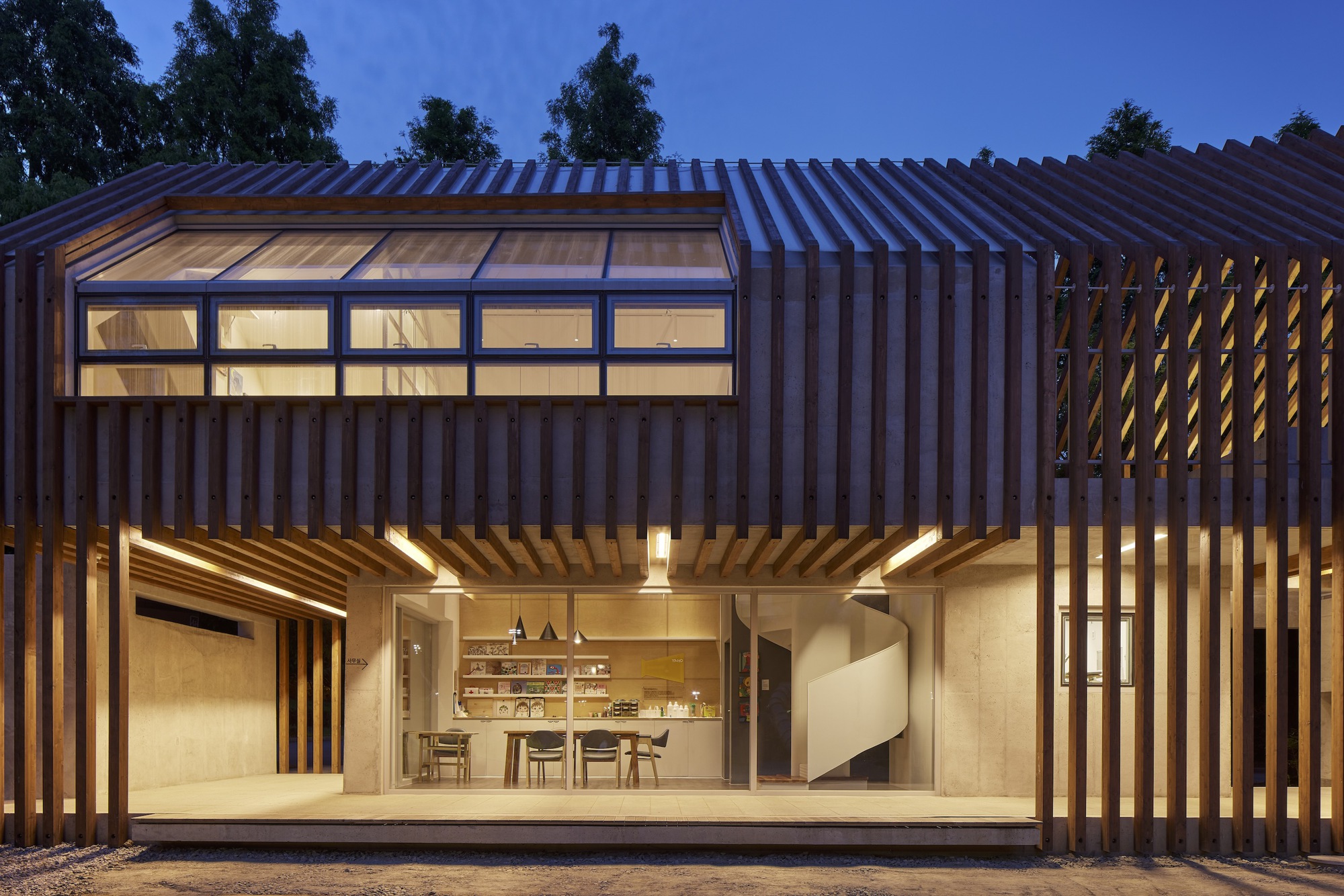 Glass-walled dining area framed by vertical timber louvers and clerestory windows at blue hour