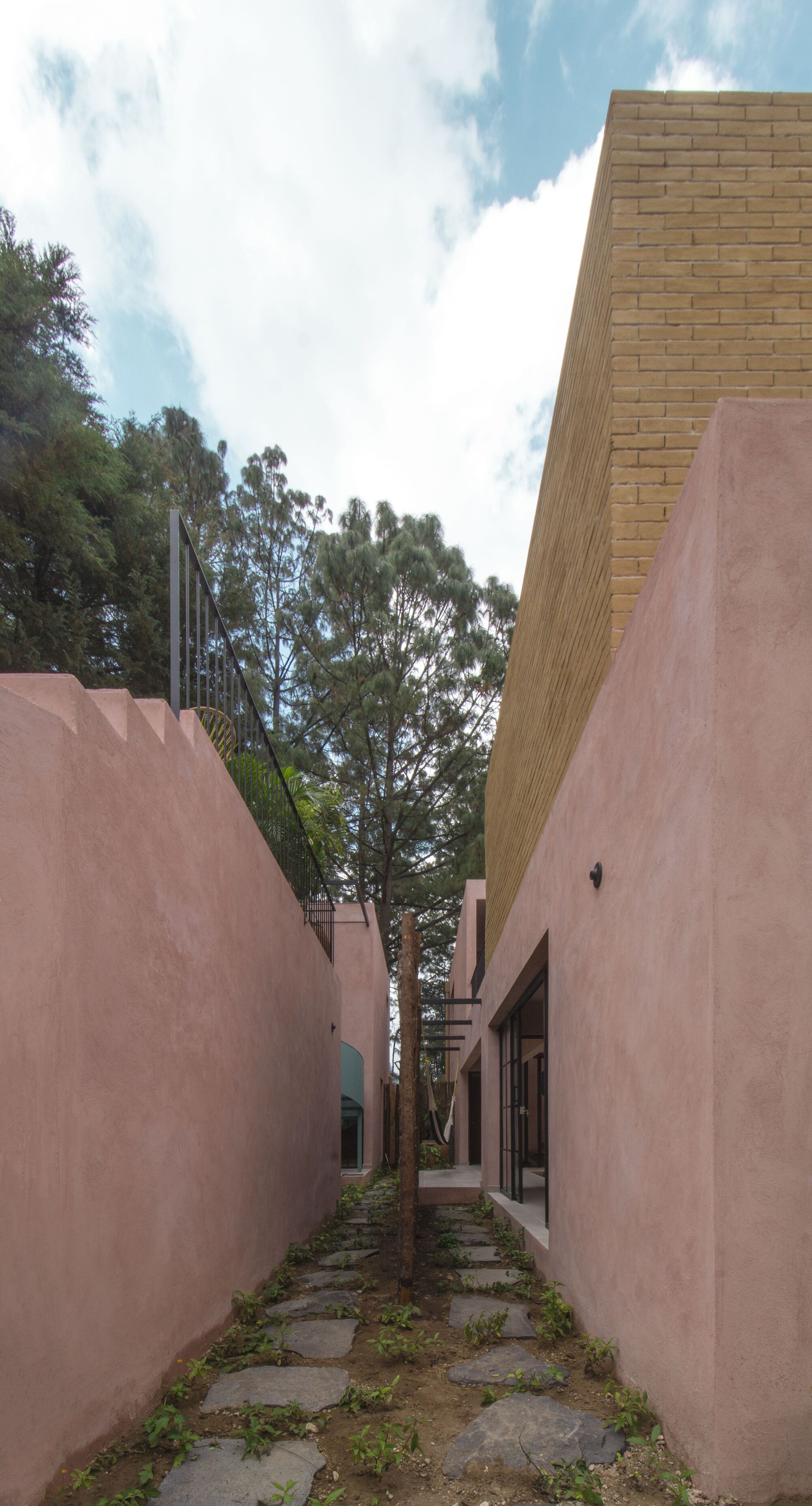 Narrow outdoor passage between pink stucco walls with stone pavers and tan brick volume above