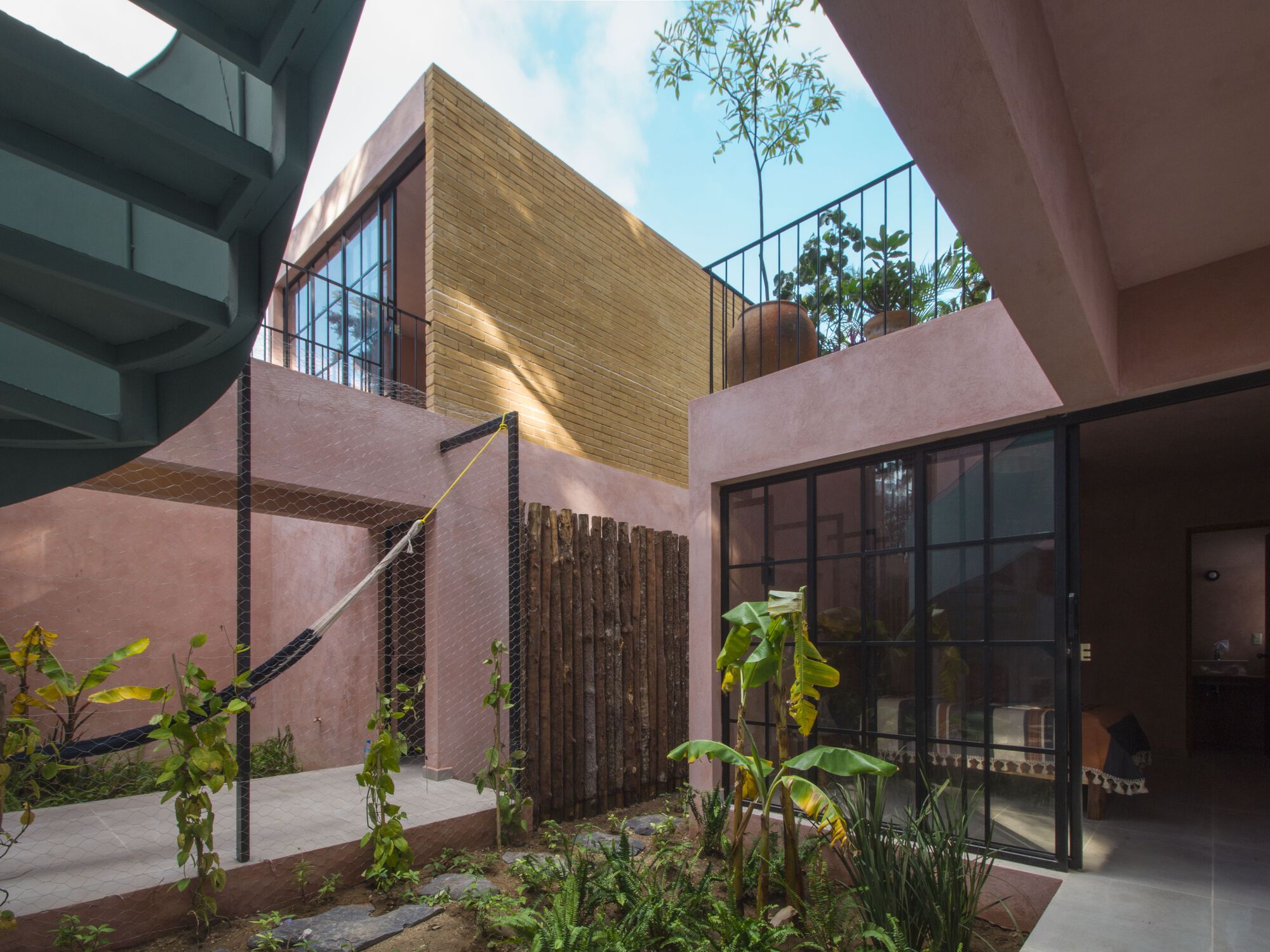 Courtyard view showing pink stucco walls, bamboo screening, glass doors, and planted beds under blue sky