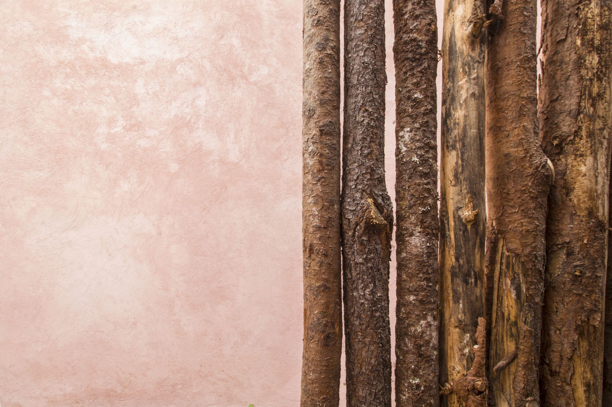 Detail of vertical bamboo poles meeting pink stucco wall at weathered junction