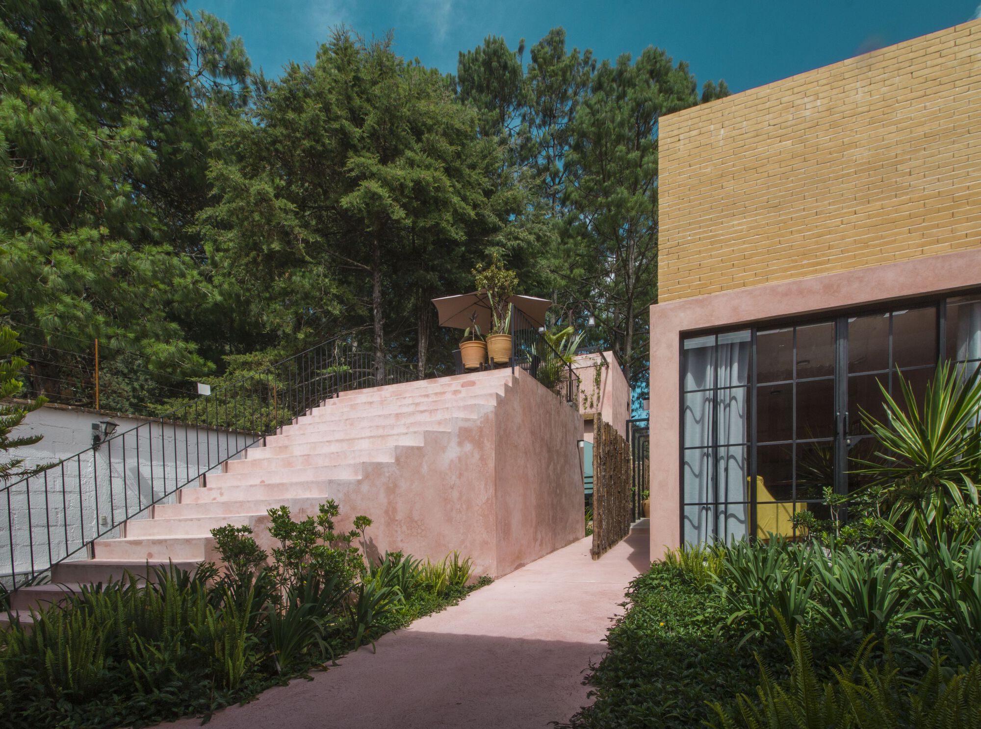 Wide pink stucco staircase ascending between planted beds with yucca and agave under blue sky