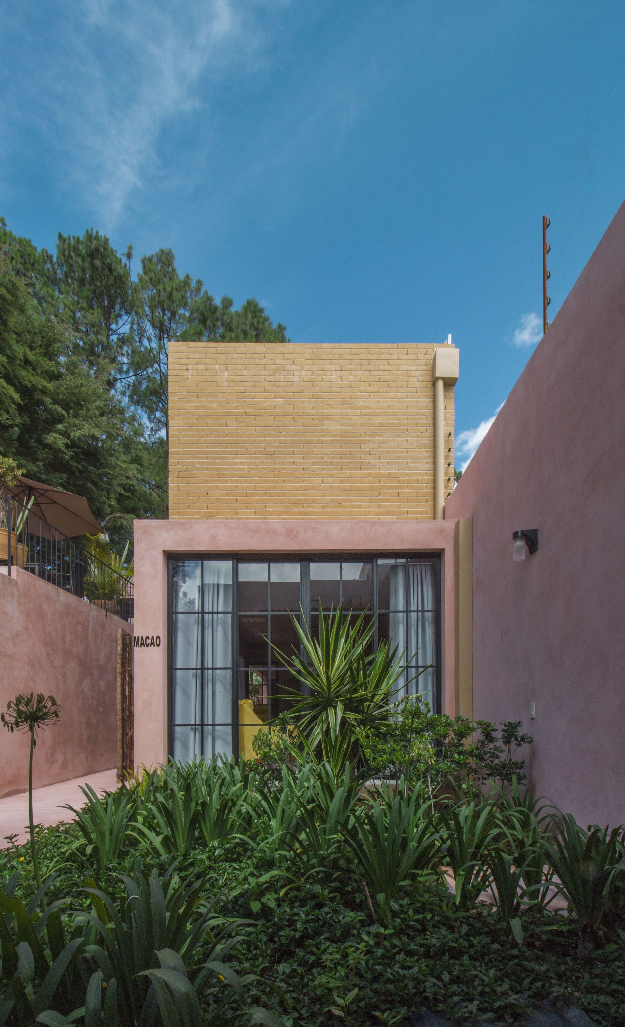 Front facade combining yellow brick upper volume and pink stucco base with black steel window grid
