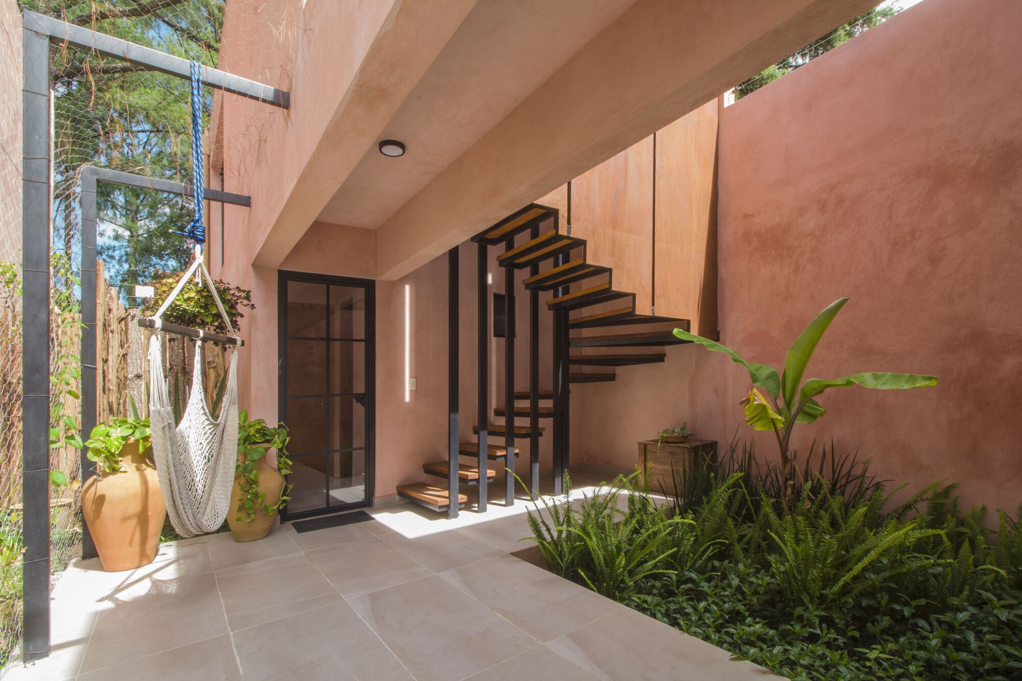 Covered terrace with open-tread steel staircase, potted plants and dappled midday sunlight