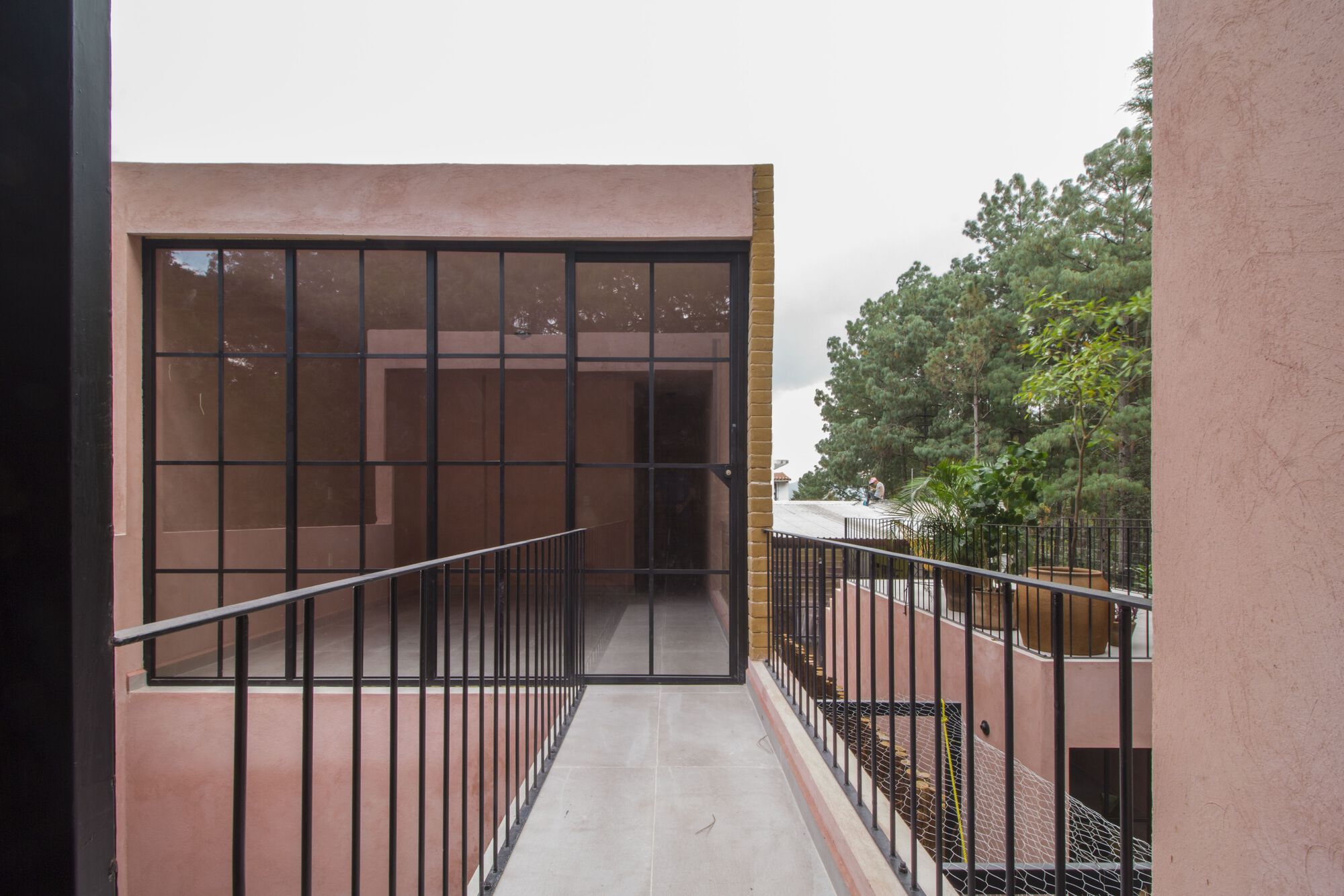 Upper-level terrace with metal railing leading to a gridded glazed wall facing surrounding trees