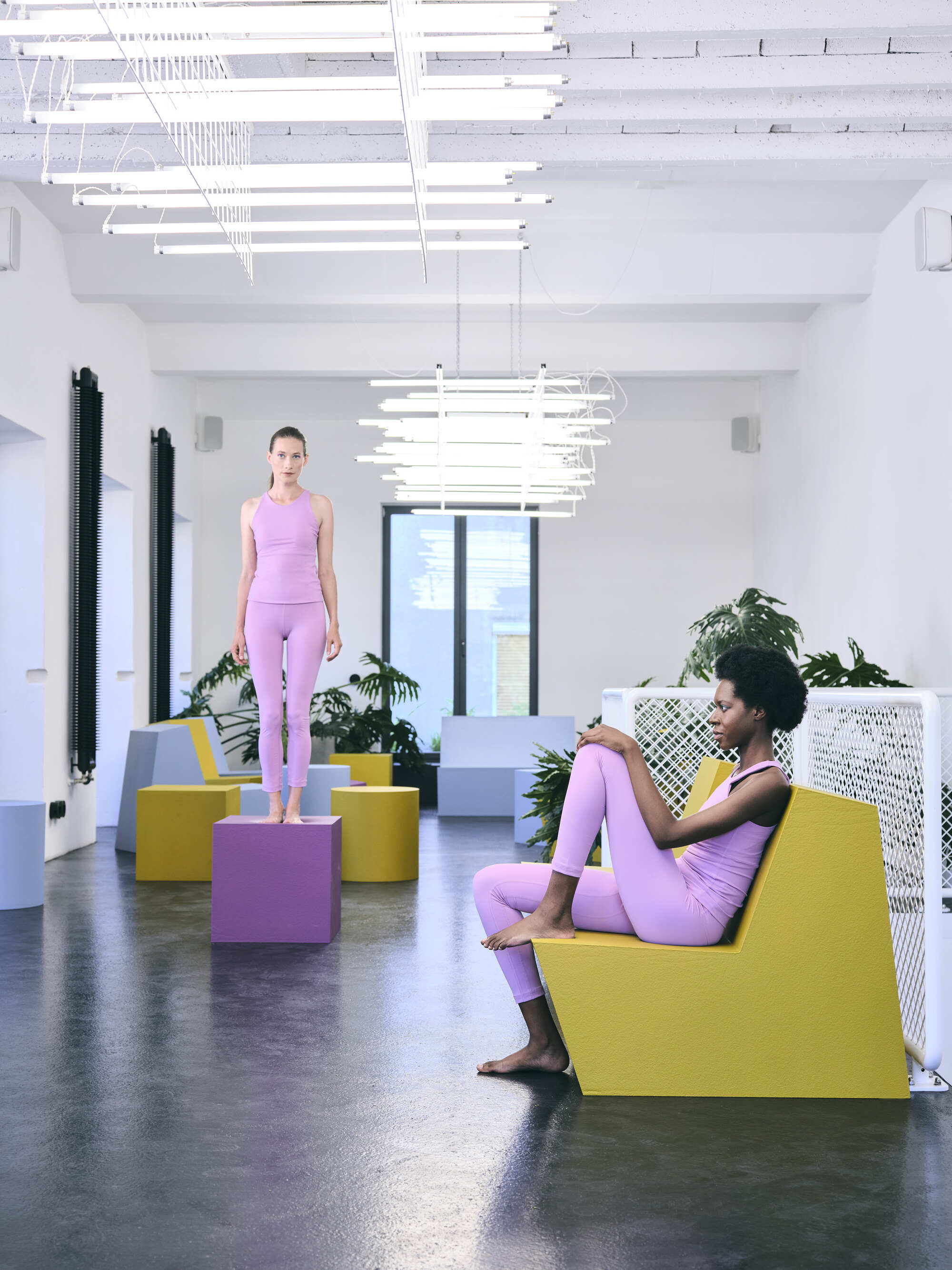 Interior room with suspended white tube lighting fixture, colored geometric seating blocks, and two occupants