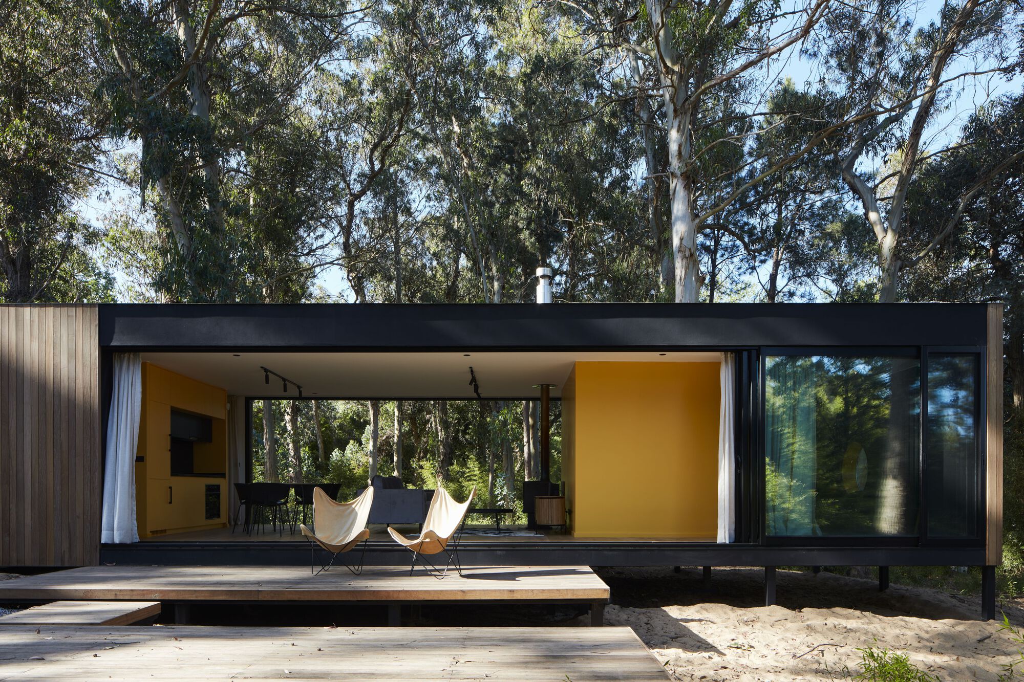 Front elevation showing the timber-clad facade with a wide covered terrace and yellow interior wall