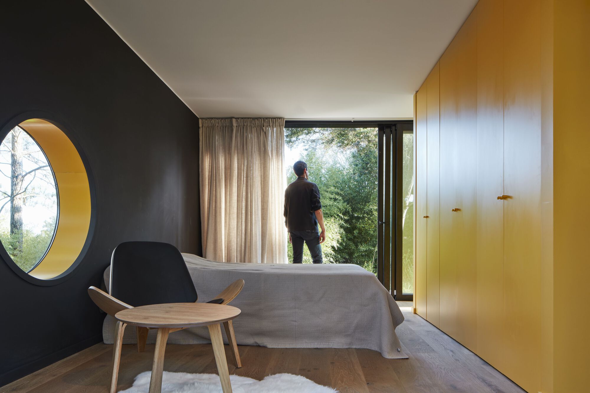Bedroom with circular yellow-lined porthole window, yellow built-in cabinetry, and figure silhouetted in glazed doorway