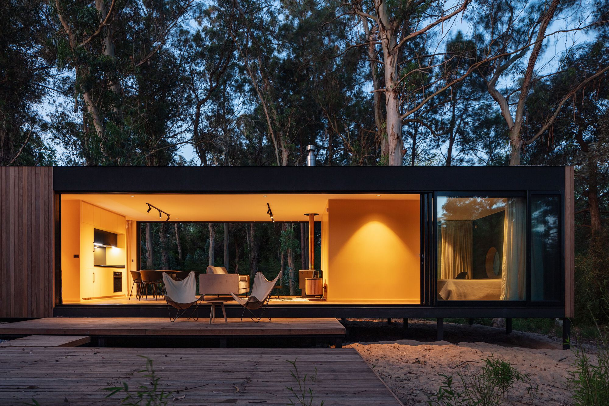 Timber deck extending from the fully glazed living volume with warm interior lighting at twilight