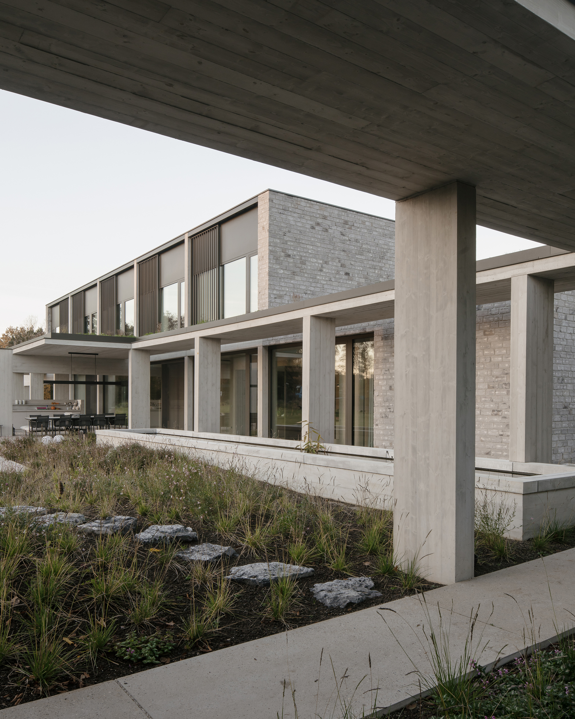 Two-story facade with concrete columns and brick walls viewed from beneath an overhanging canopy at dusk