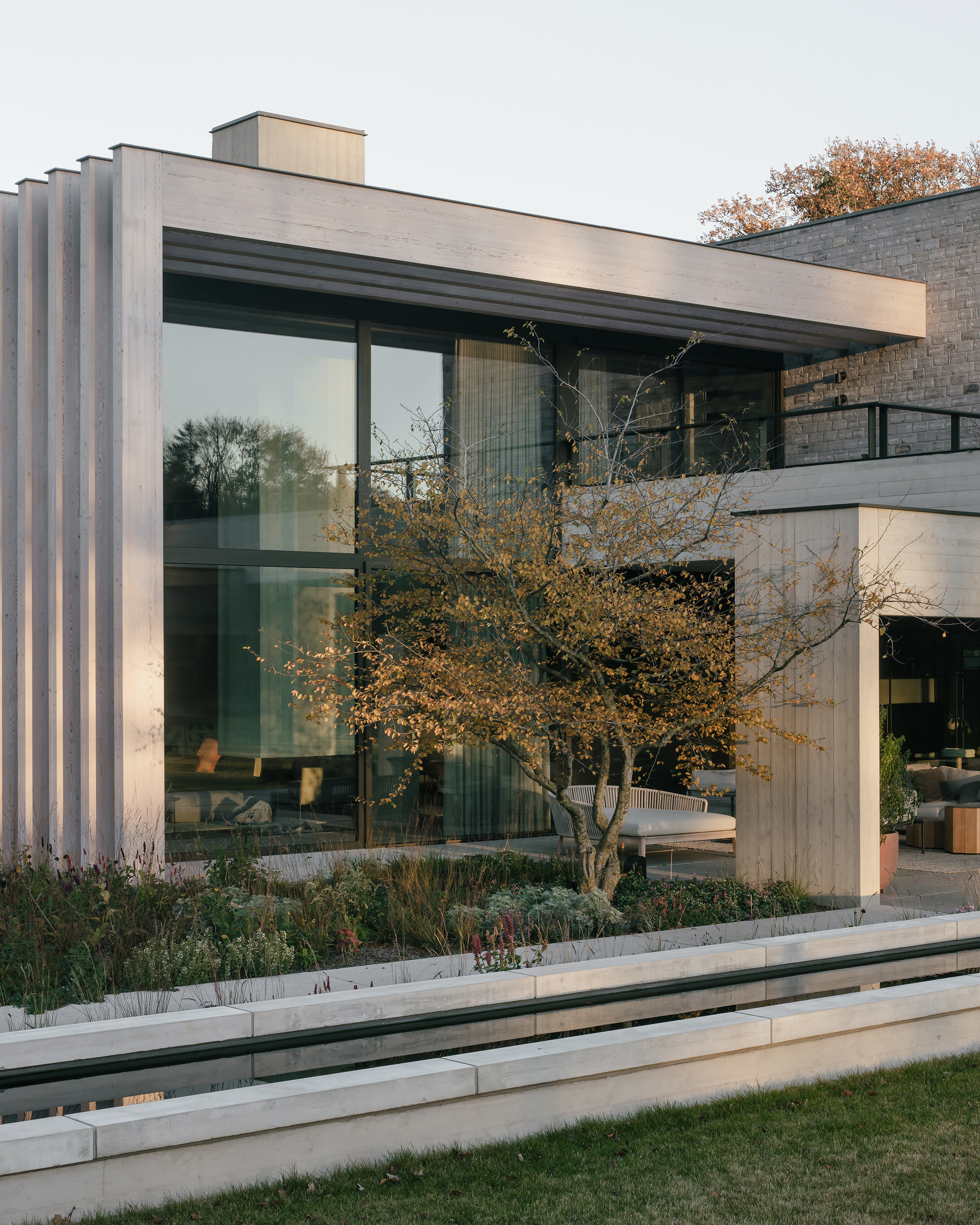 Garden facade with full-height glazing, vertical timber screening and a mature tree in autumn foliage