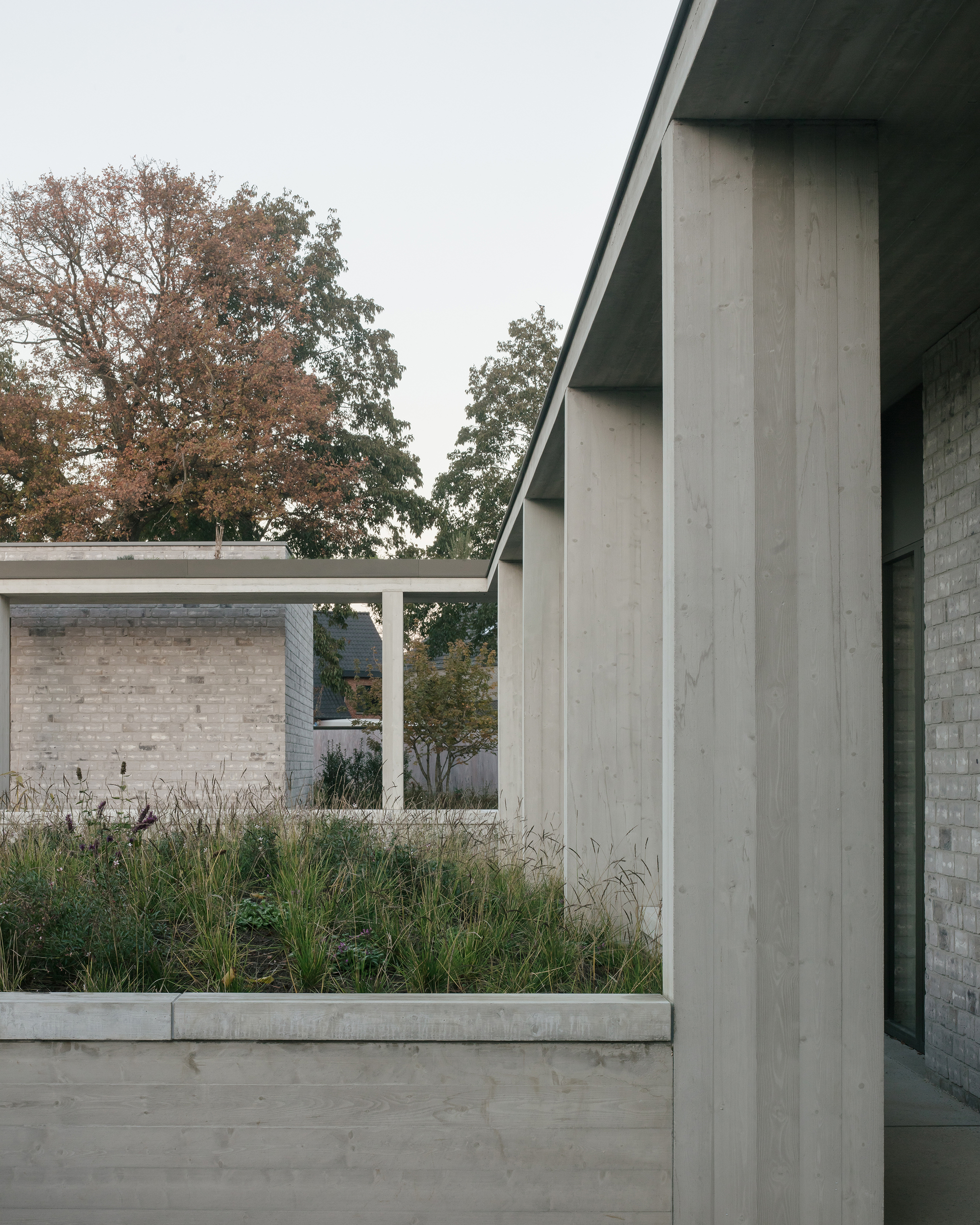 Concrete columns framing a planted bed with ornamental grasses beneath an autumn canopy