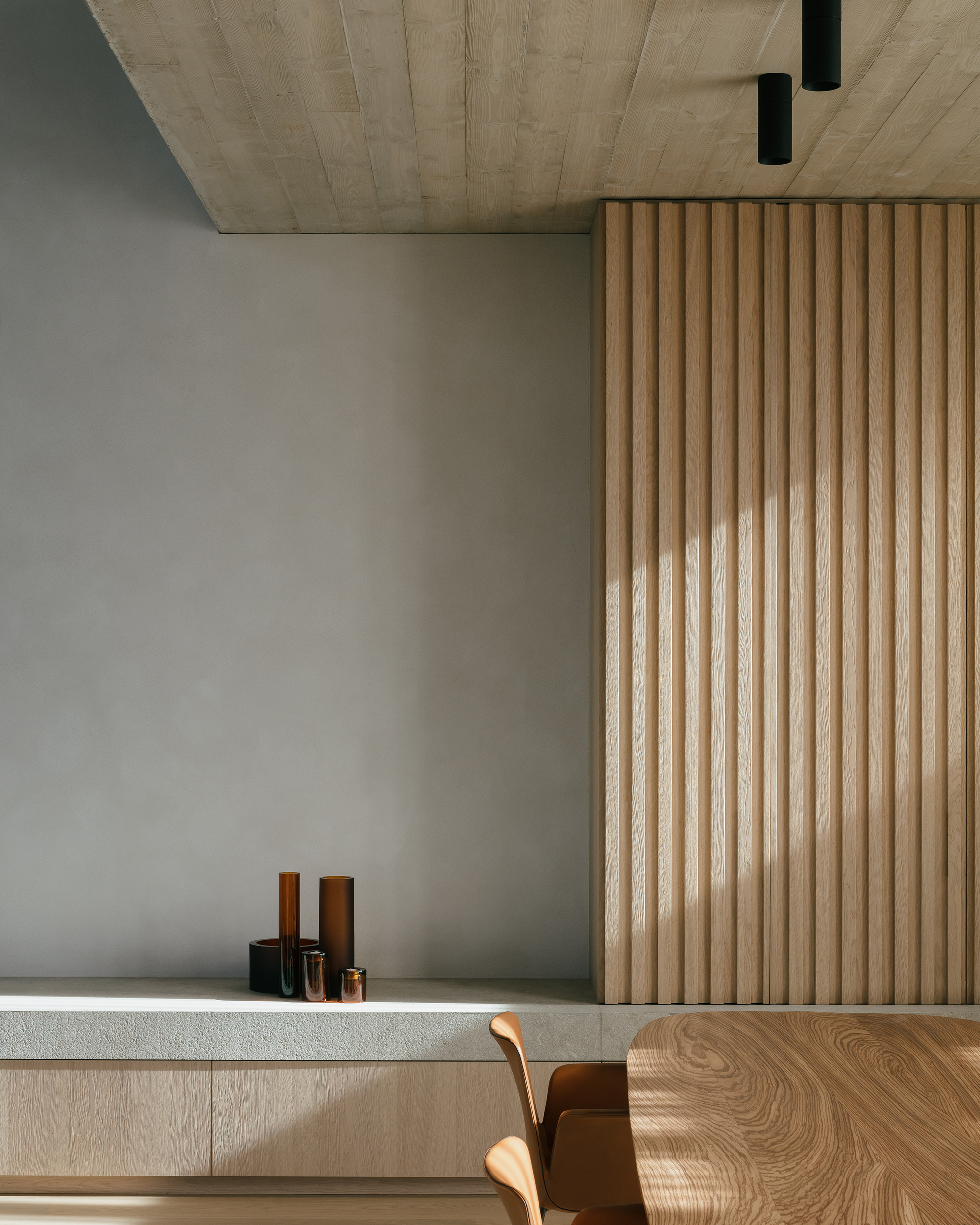 Interior view showing vertical timber slat partition beside a dining table with exposed concrete ceiling above