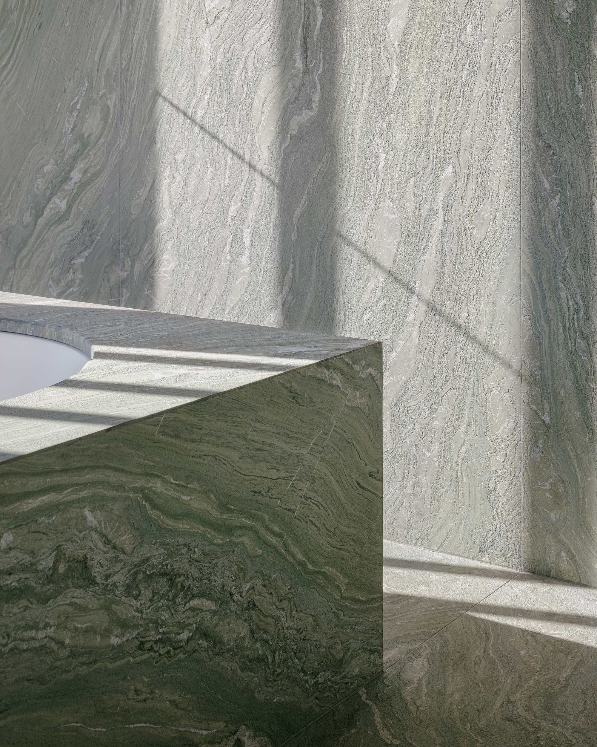 Green veined marble block meeting pale stone wall with angular shadows cast across the surfaces