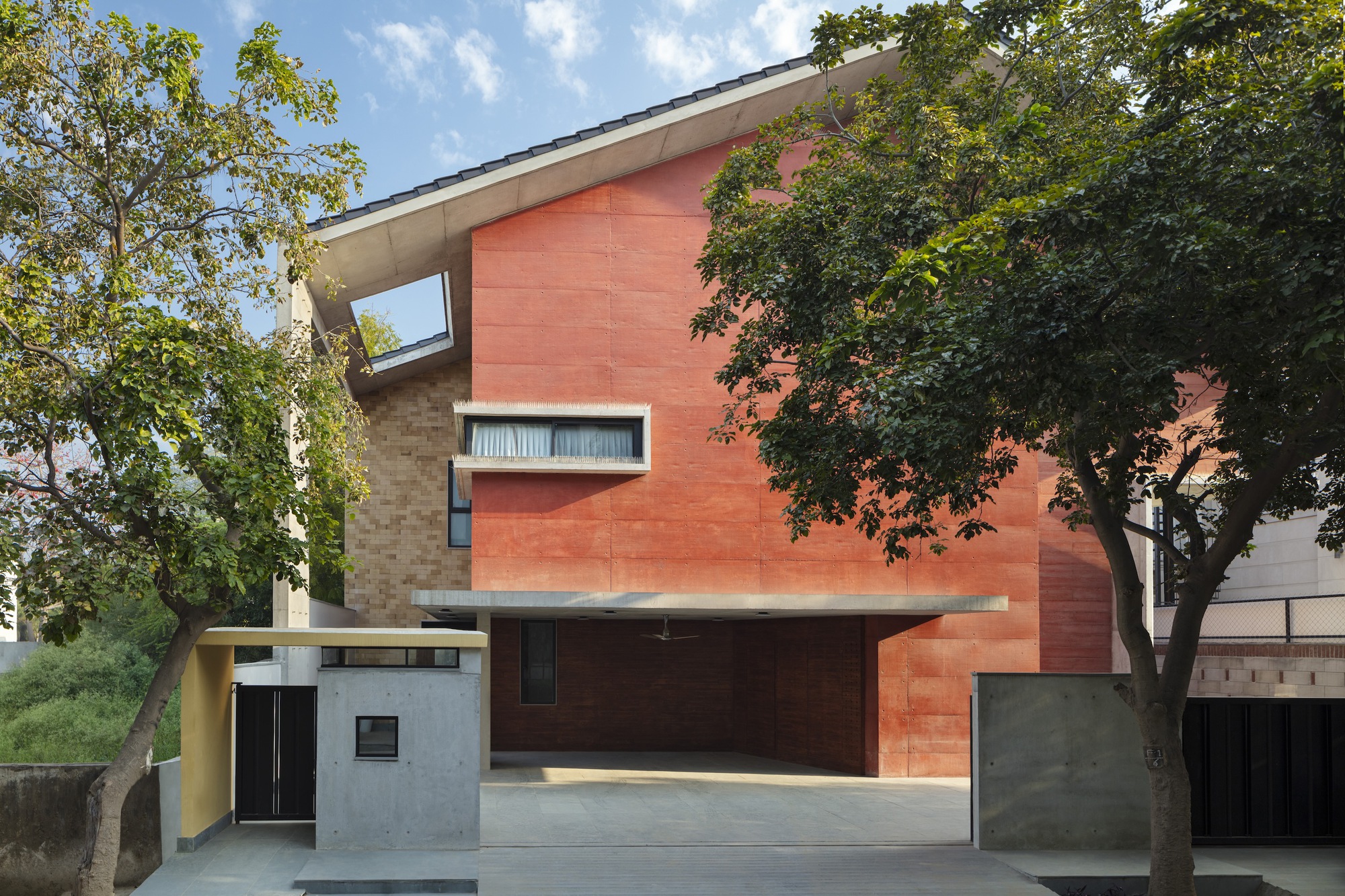Street view of the red sandstone facade with narrow windows framed by mature trees on both sides