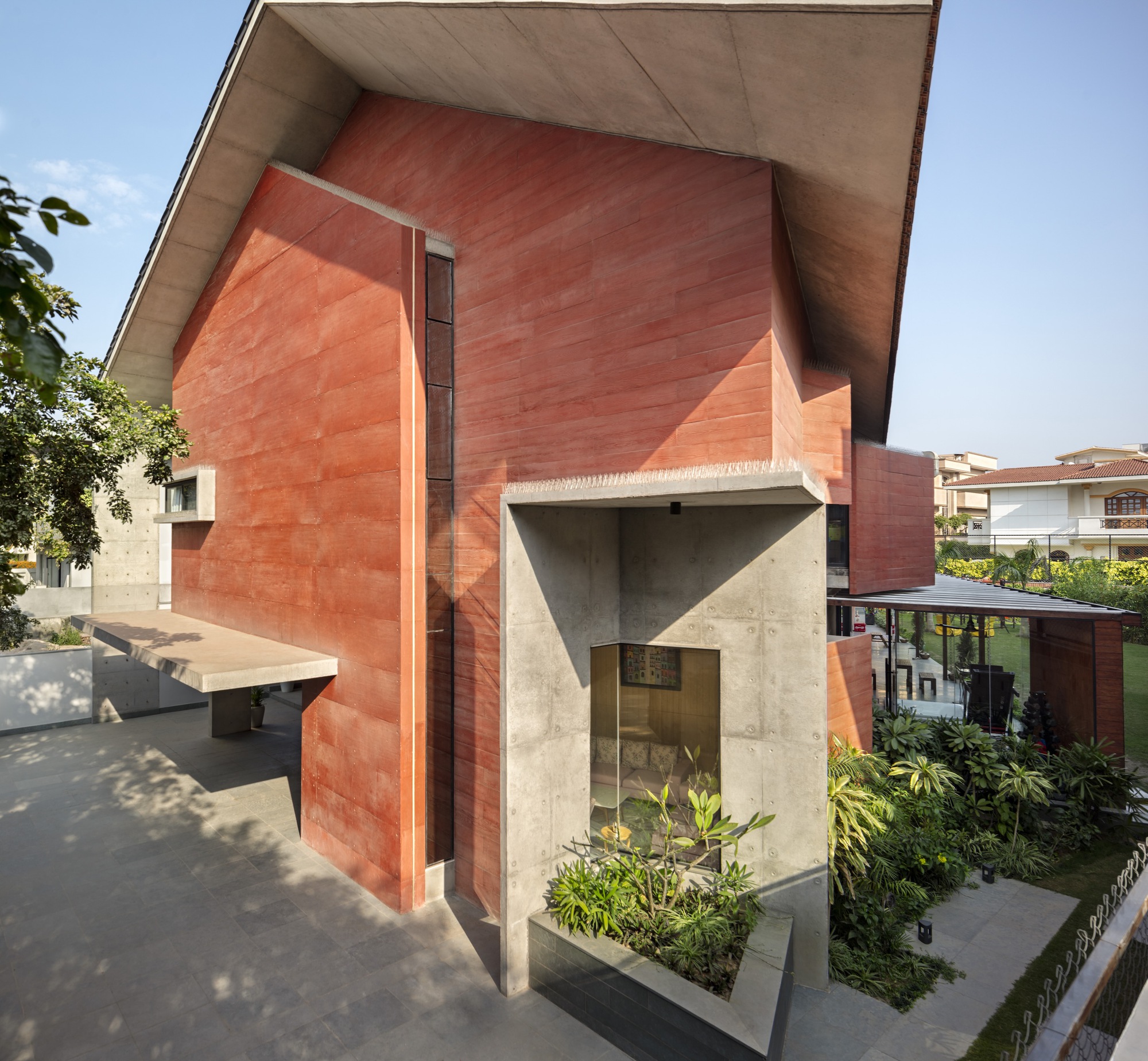 Red sandstone volumes with a concrete entry portal and planted courtyard below in afternoon light