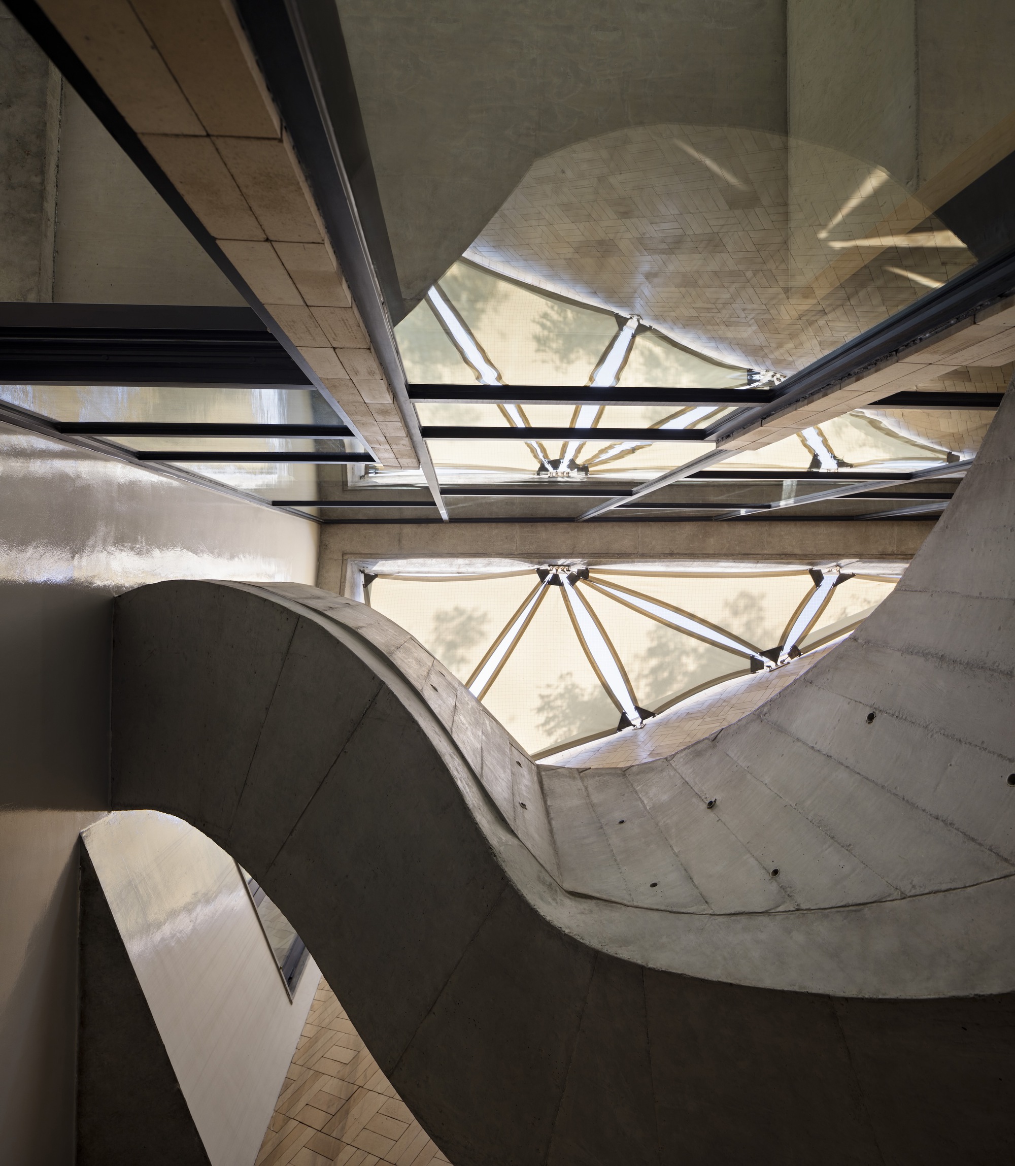 View looking up at the concrete stairwell with triangular skylights and steel bracing overhead