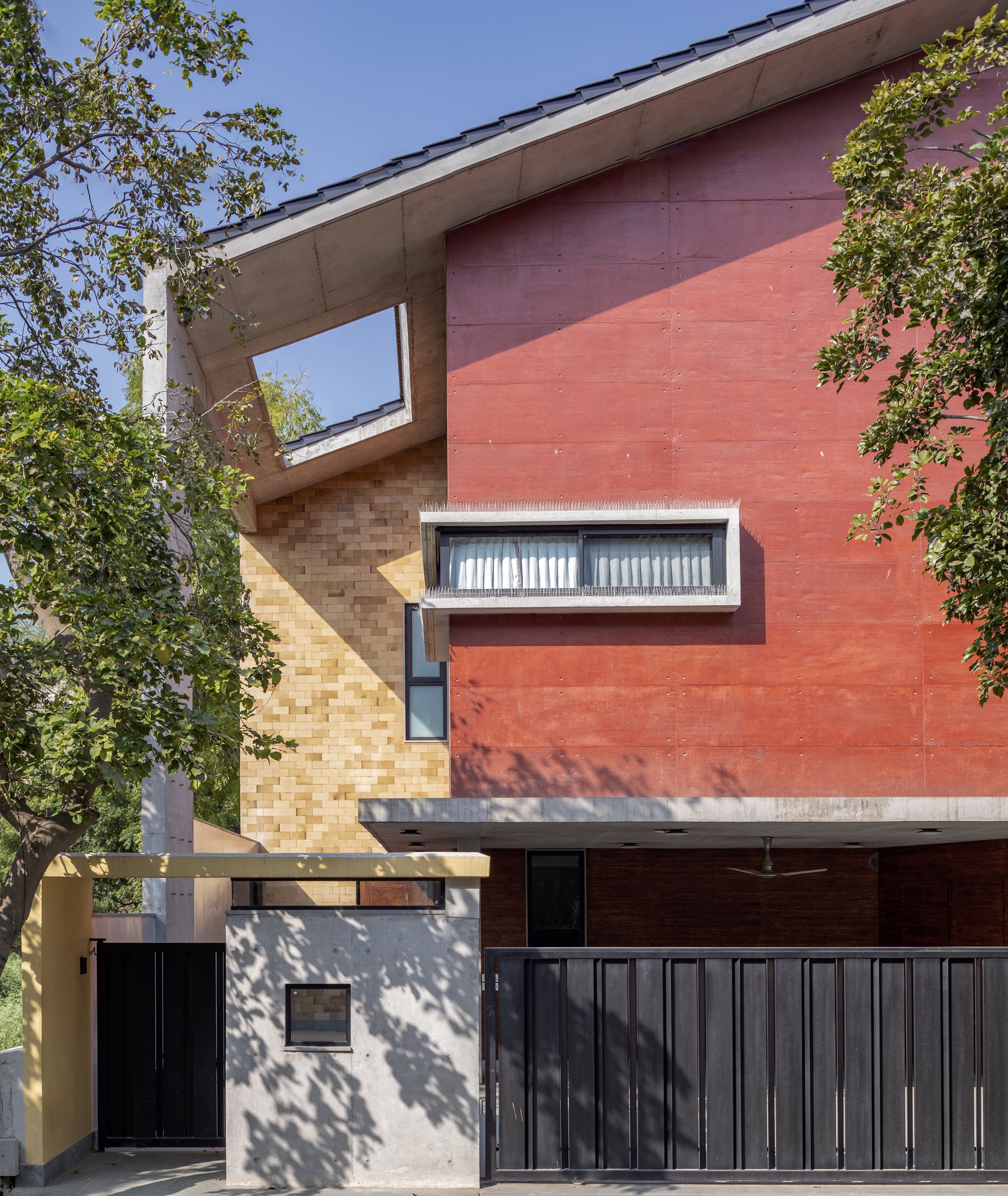 Red sandstone and ochre brick facade with horizontal window band and tree shadows on the entry wall