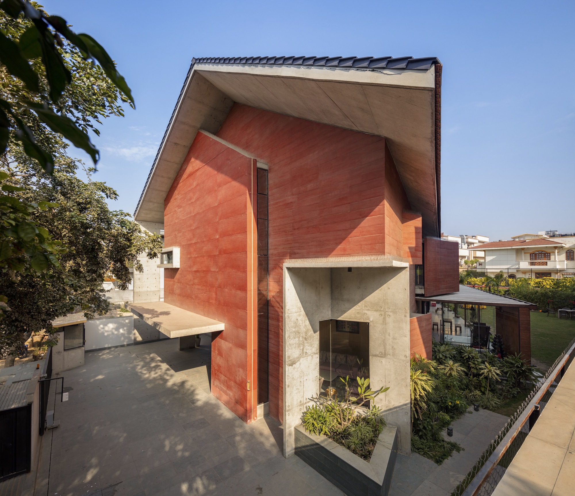 Red volcanic stone facade with angular concrete entry canopy and planted beds under a blue sky