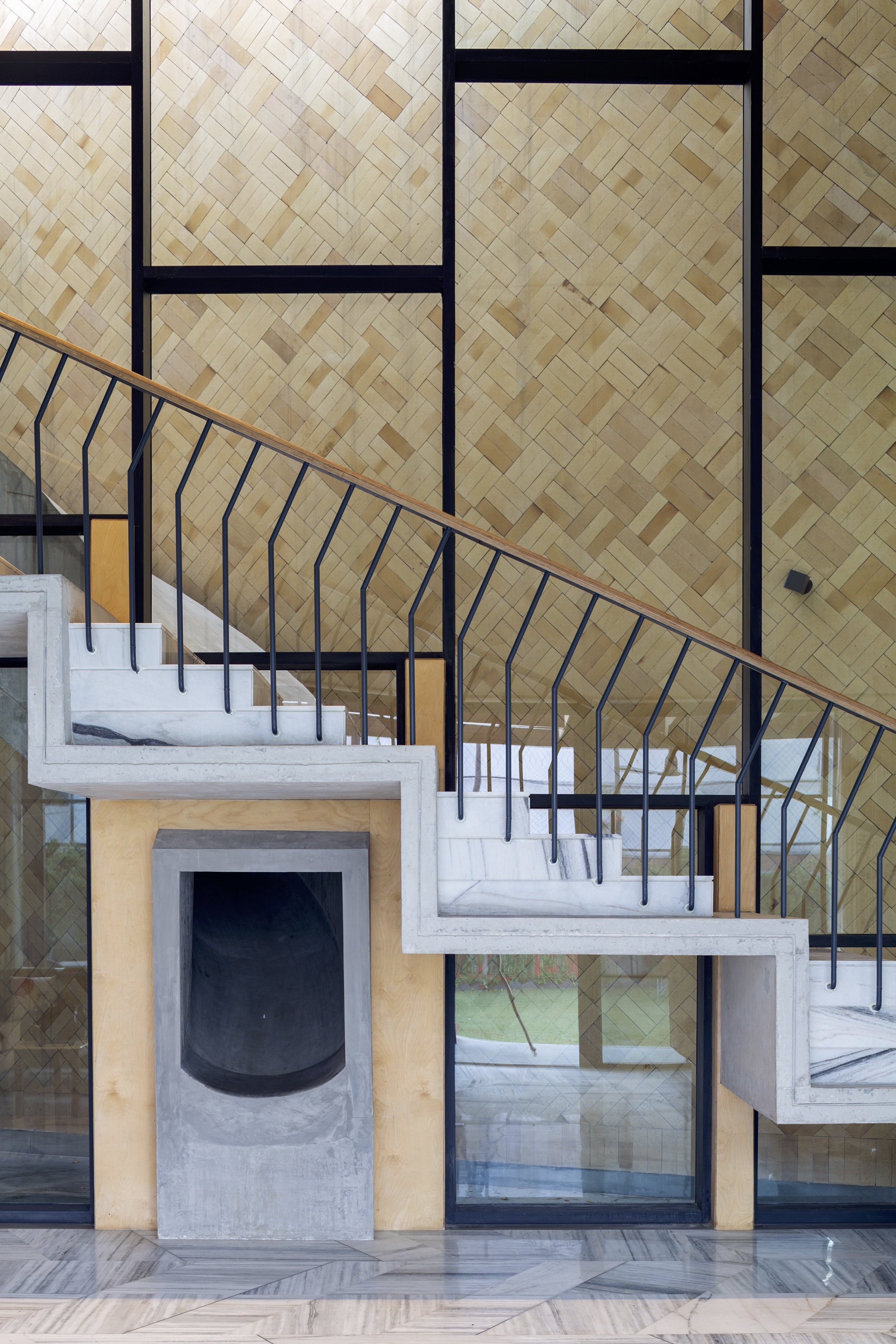 Black metal staircase with curved railing rising past herringbone bamboo wall panels and fireplace surround