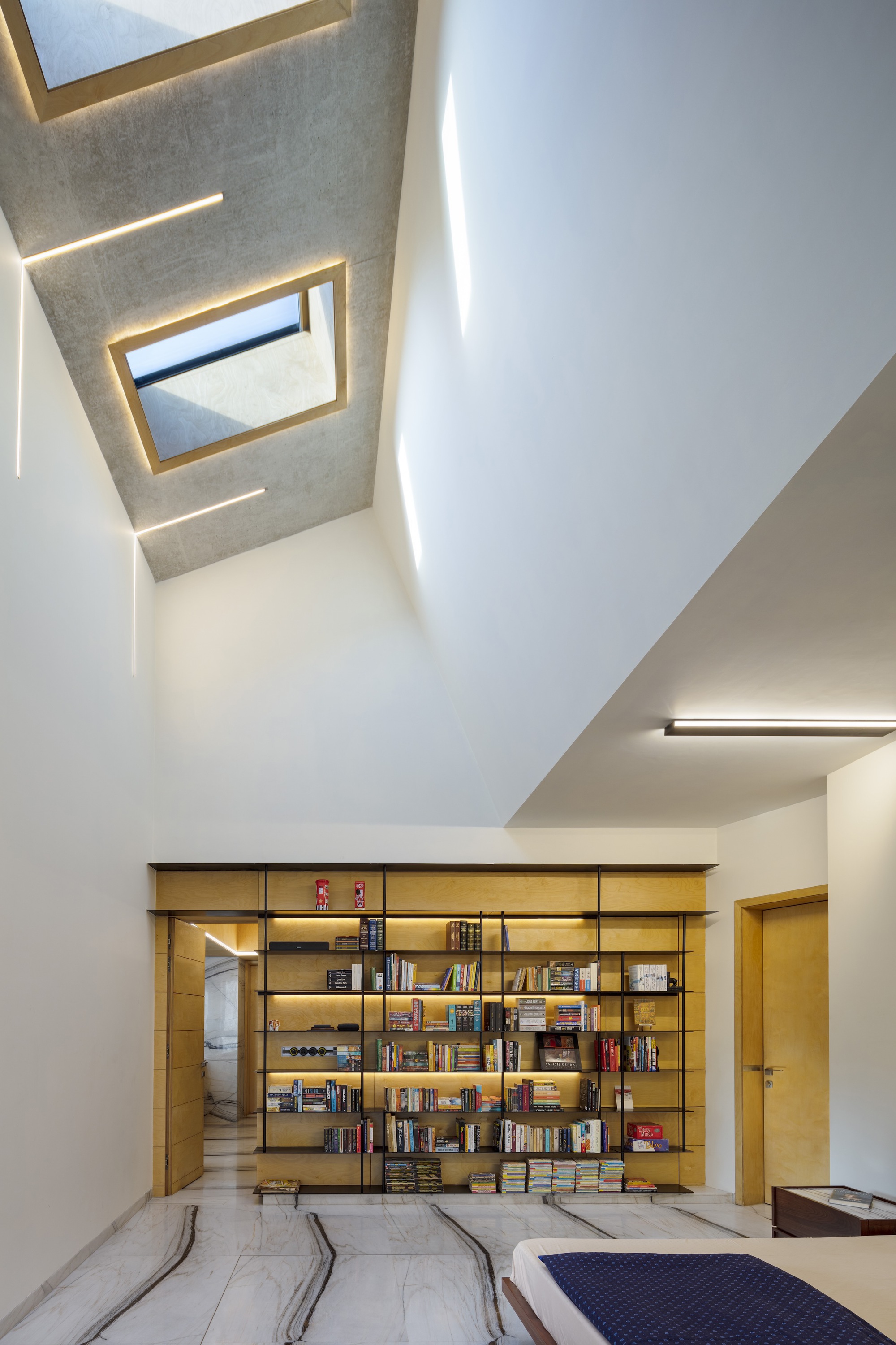 Double-height library space with skylights, timber bookshelves, and recessed cove lighting along white walls