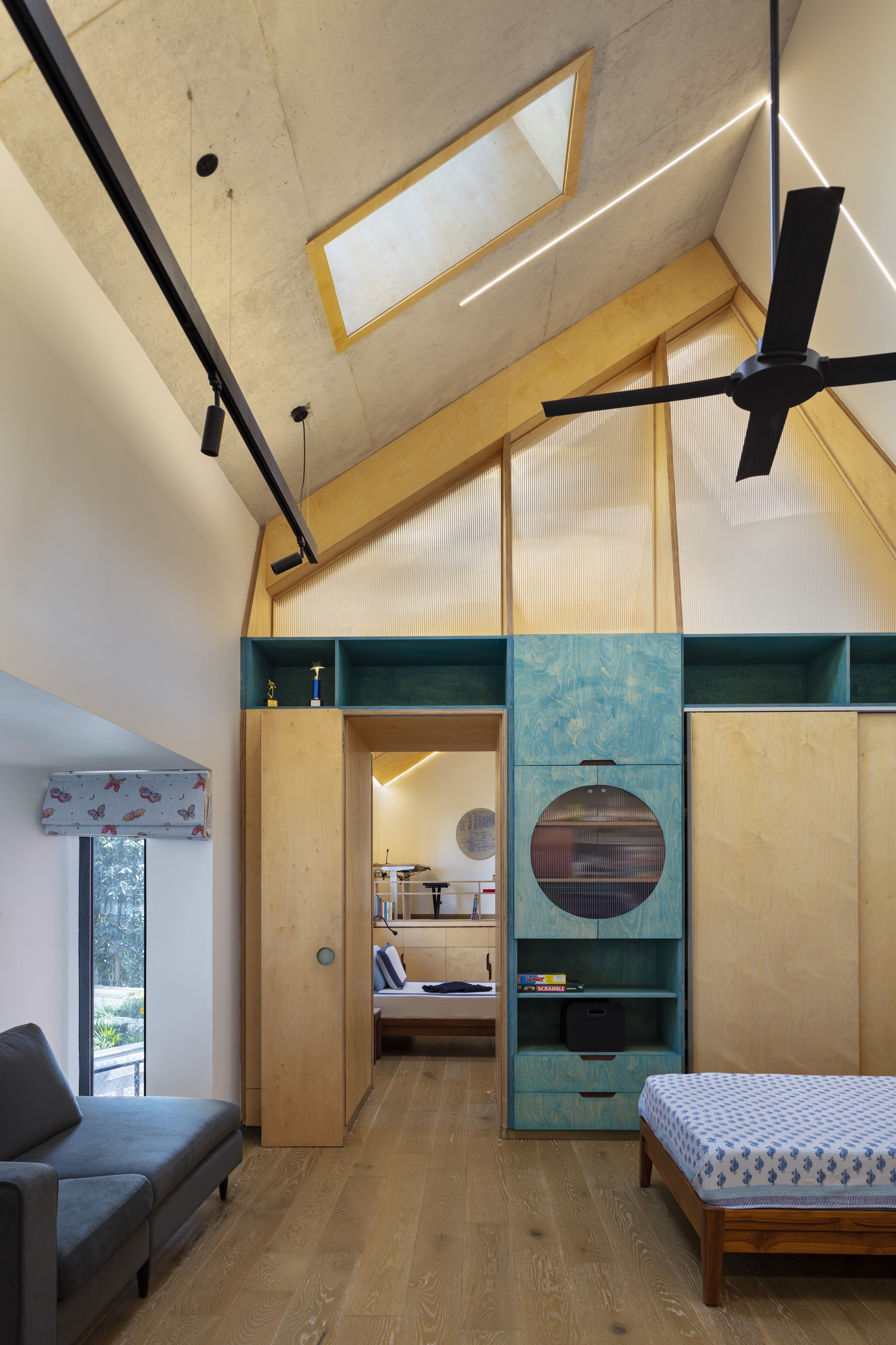 Vaulted bedroom interior with plywood storage unit featuring circular porthole openings and integrated green shelving