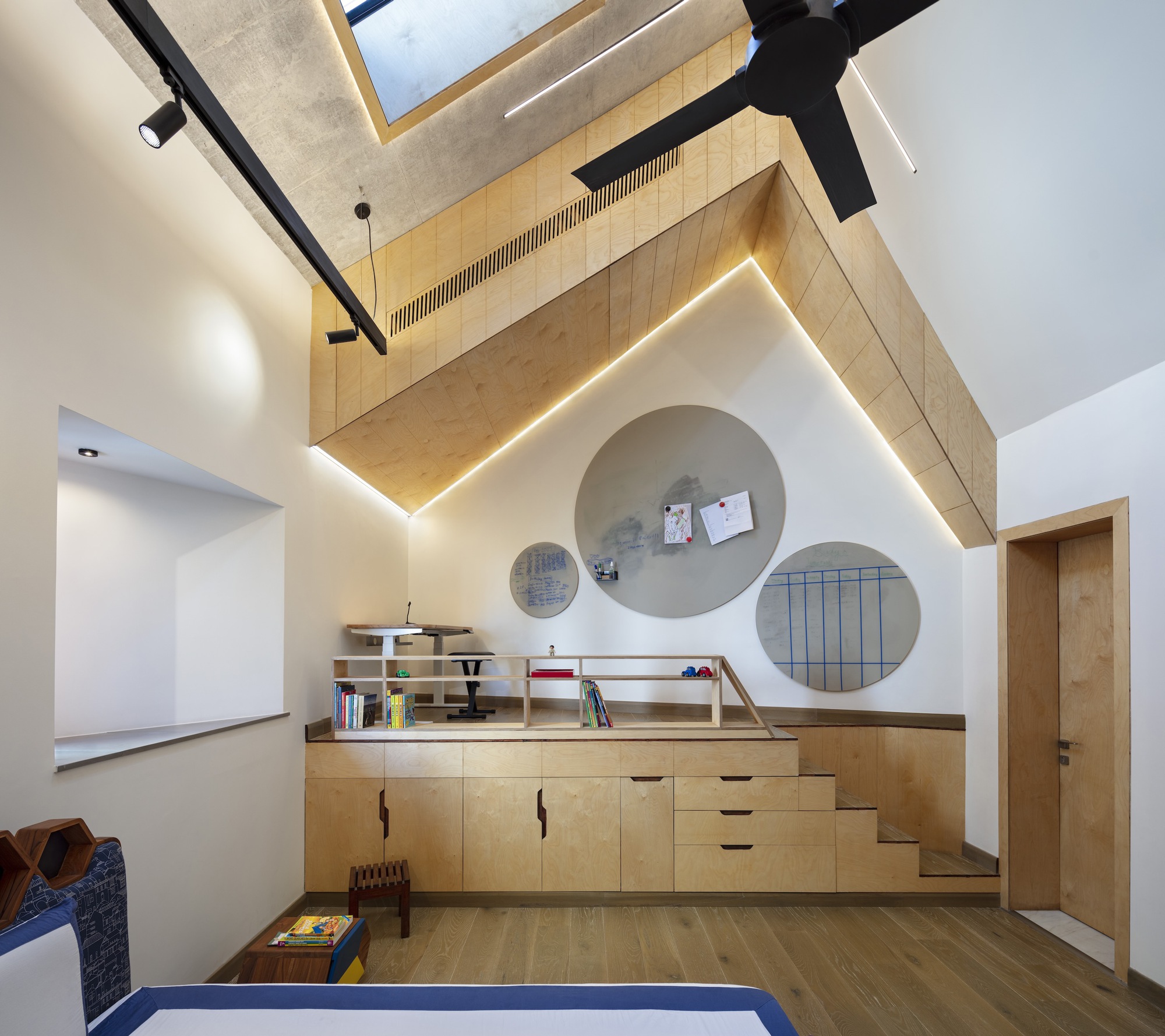 Plywood loft platform with circular wall niches and built-in storage cabinets under a vaulted ceiling