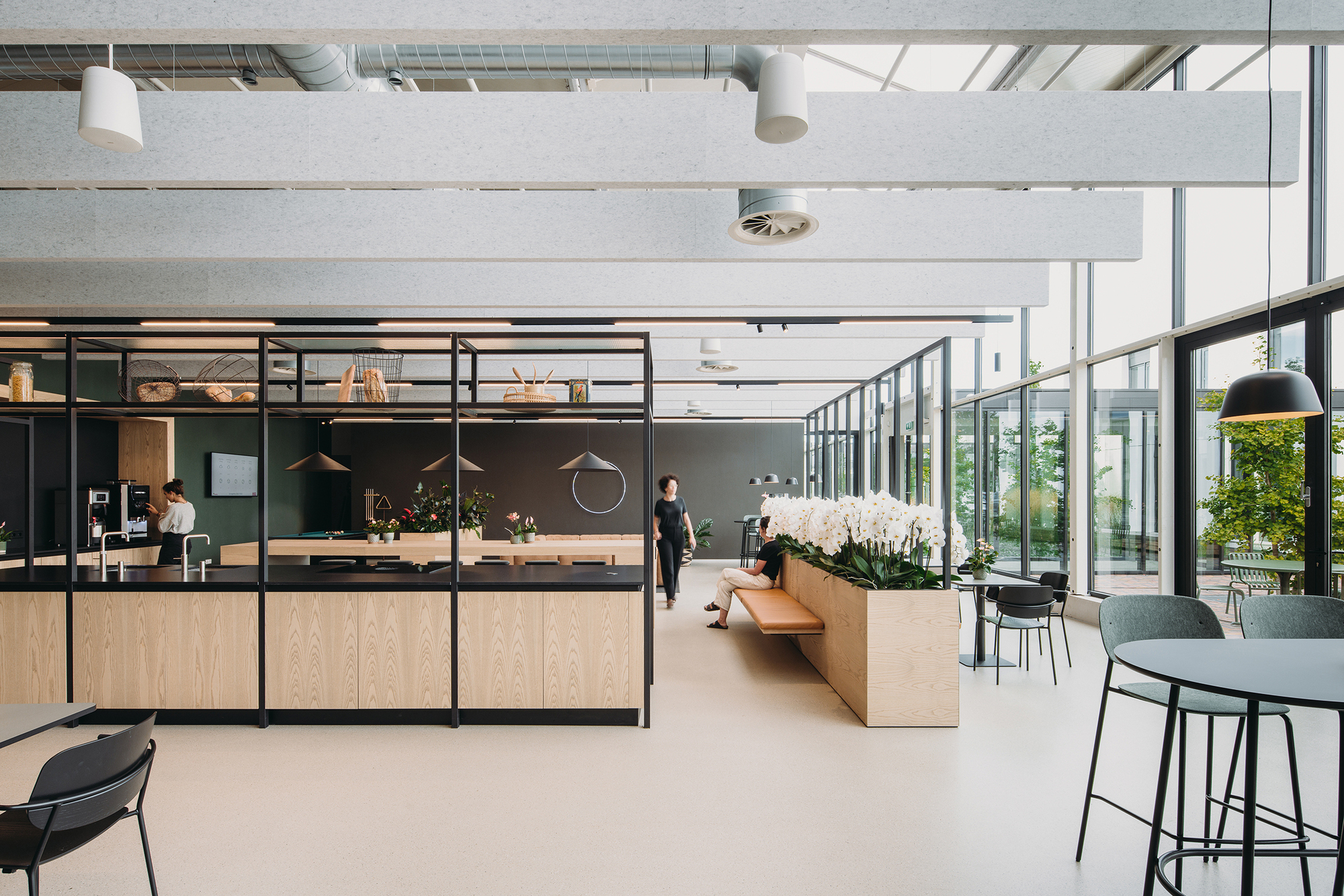 Open-plan canteen with glazed black-framed partitions and exposed ceiling beams