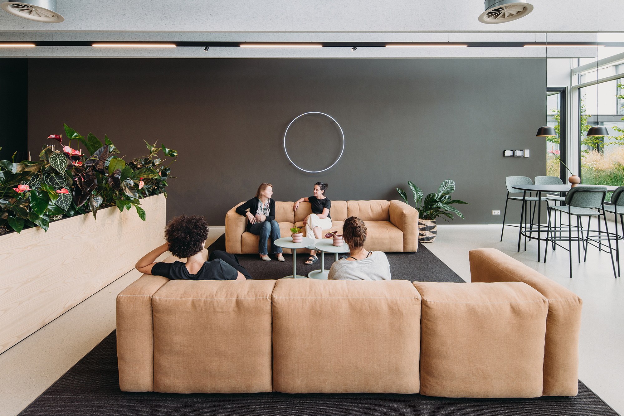 Lounge area with tan modular sofas, dark grey accent wall, and people gathering around low coffee tables