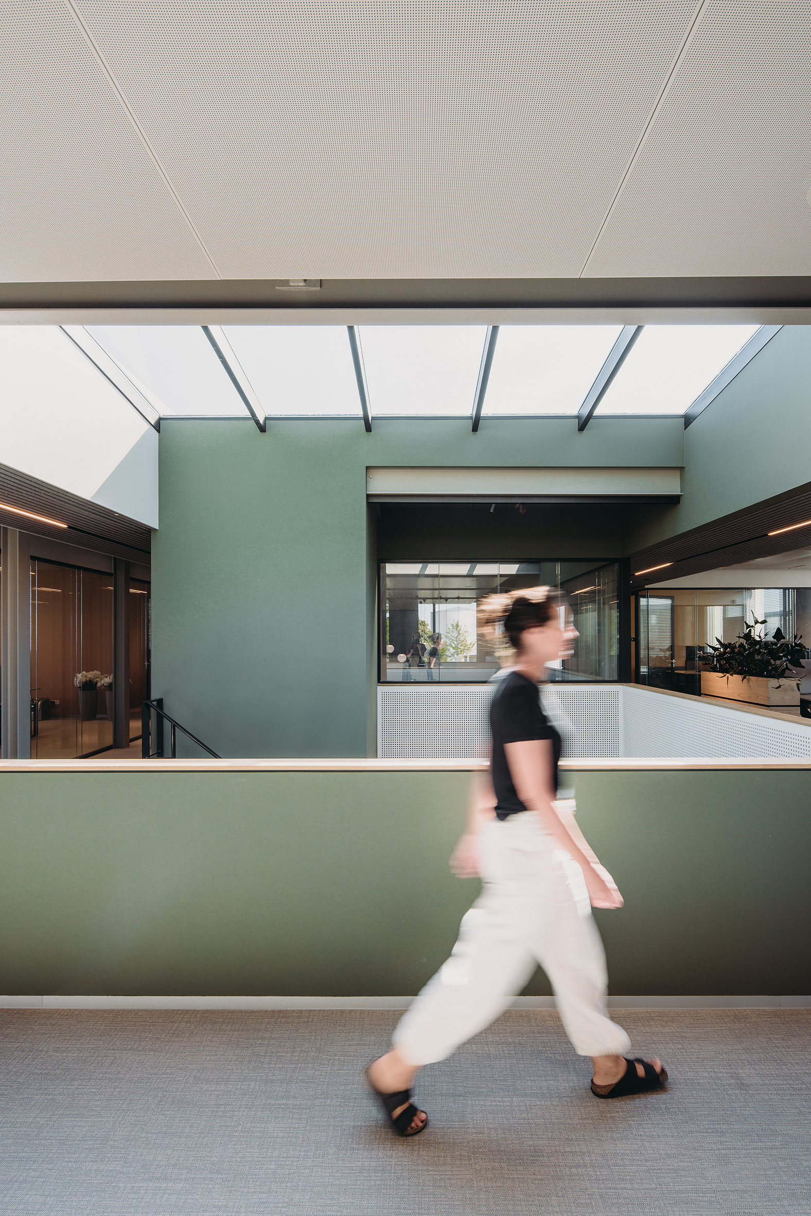 Mezzanine walkway with mint green guardrail and a person in motion beneath perforated ceiling panels